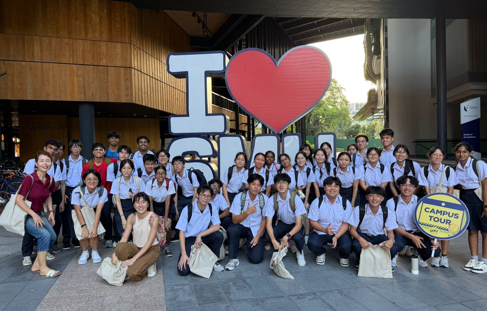 A large group of uniformed students poses in front of an I Love SMU sign during a campus tour.