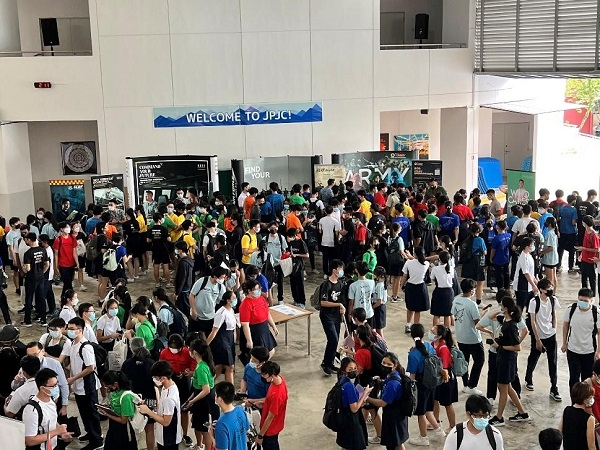 Large crowd of students in colorful shirts gathered indoors under a "Welcome to JPJC!" banner with Army recruitment displays.