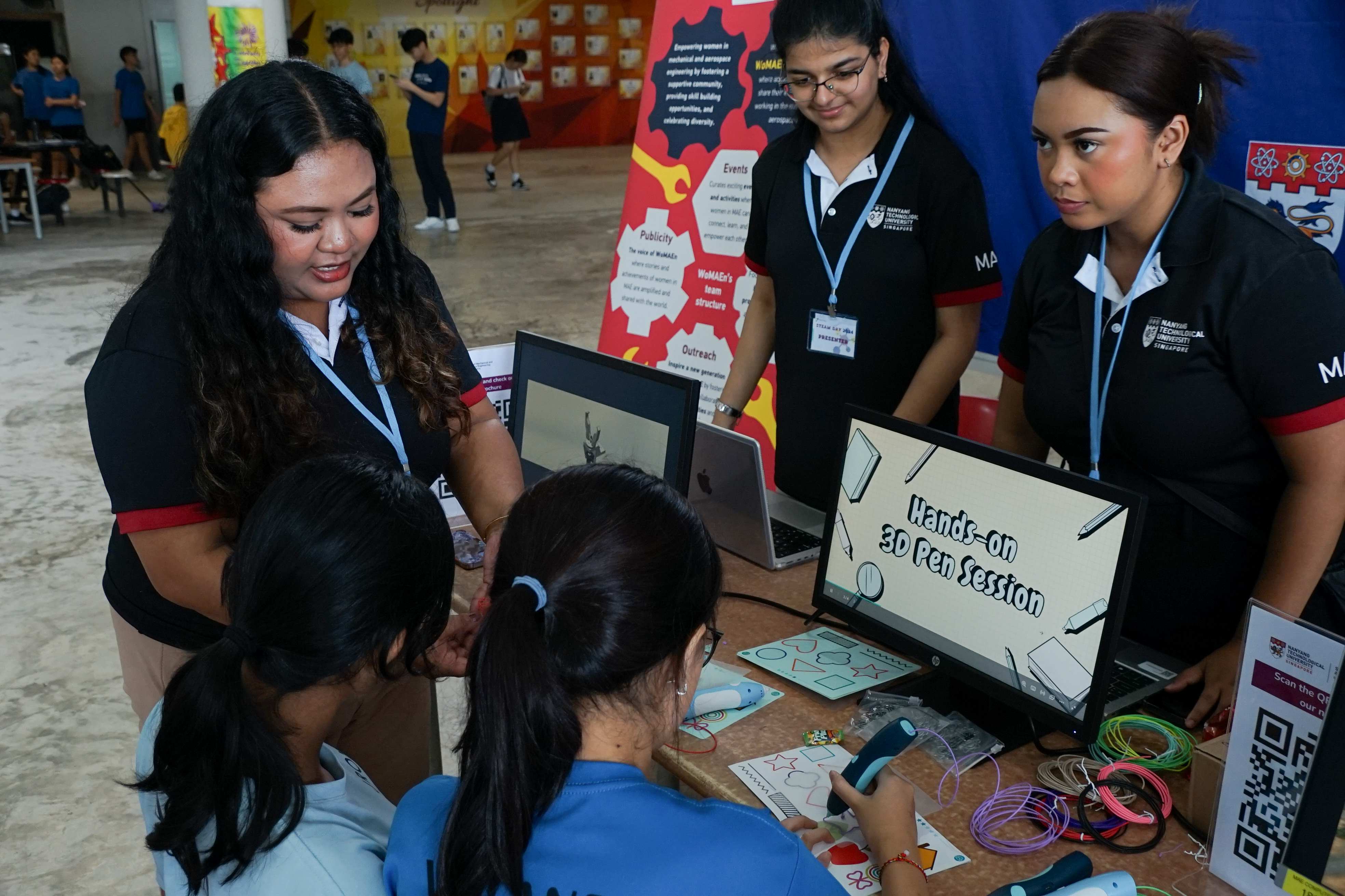 Students gather at a booth for a hands-on 3D pen session, with a monitor displaying the activity title.