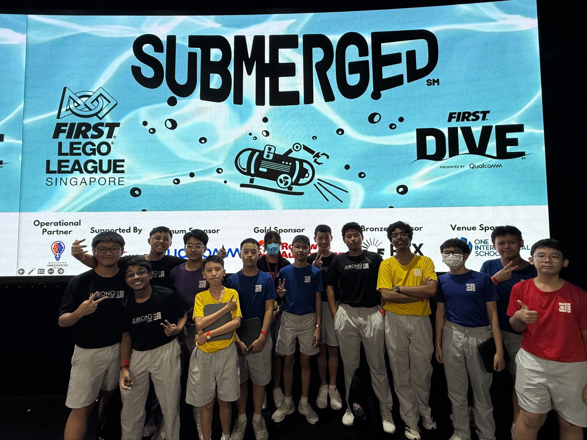 A group of young students posing in front of a FIRST Lego League Singapore Submerged event banner.