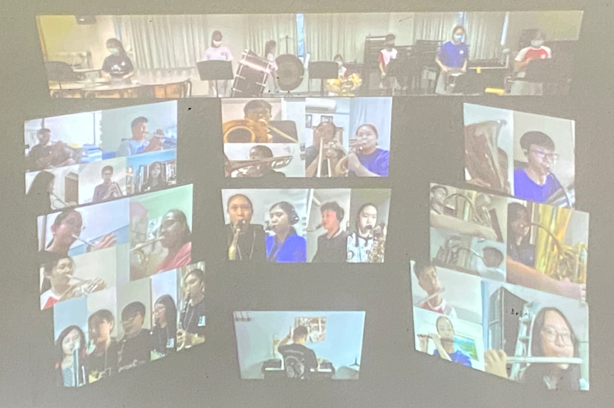 A projected collage of multiple video clips showing students playing brass and wind instruments during a virtual music session.