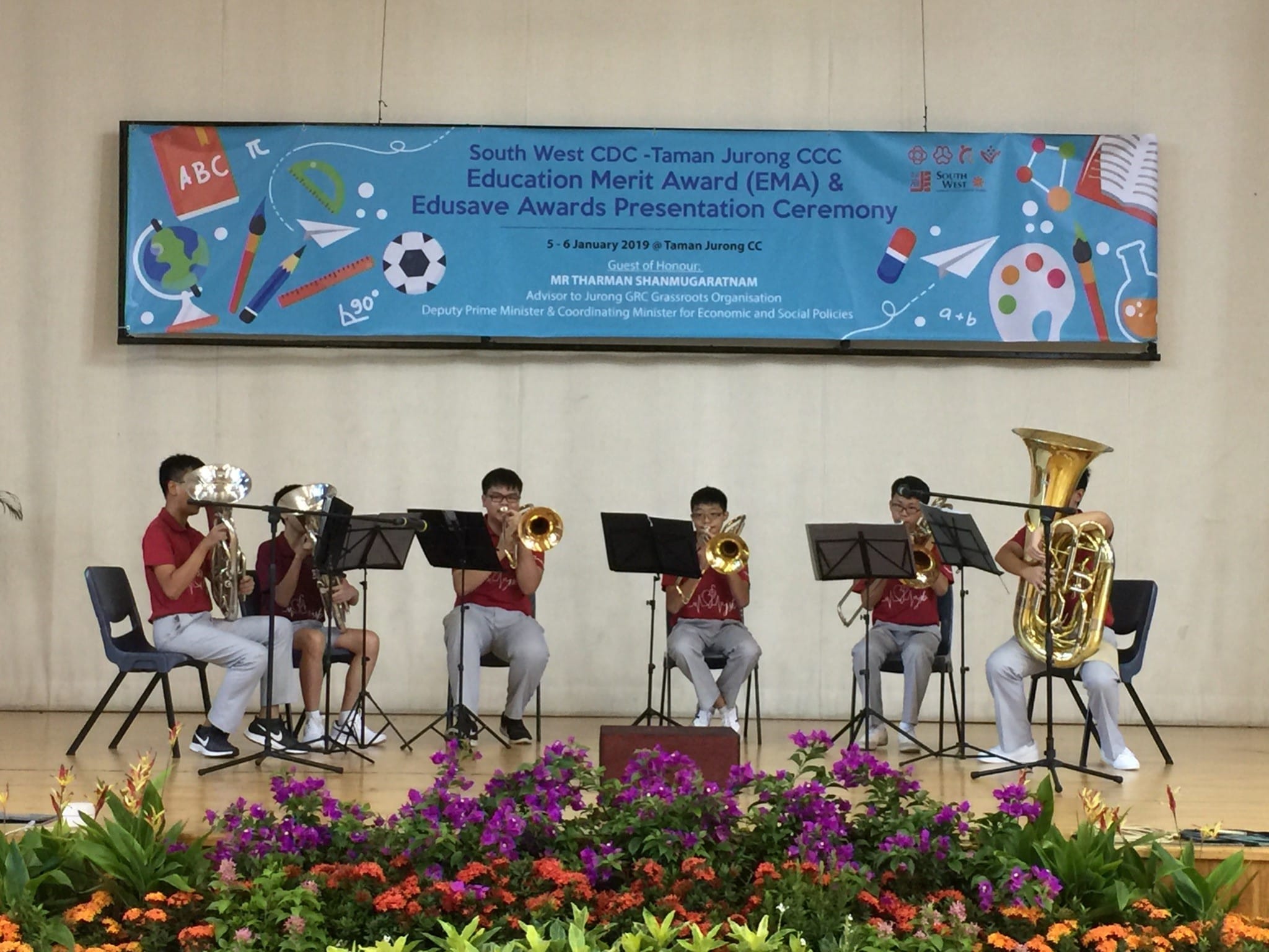 Six students in red shirts play brass instruments on a stage at a South West CDC Edusave Awards ceremony.