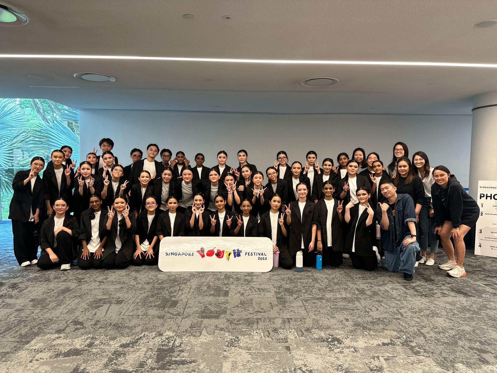 Large group of young people in black and white outfits posing with a Singapore Youth Festival 2025 sign.