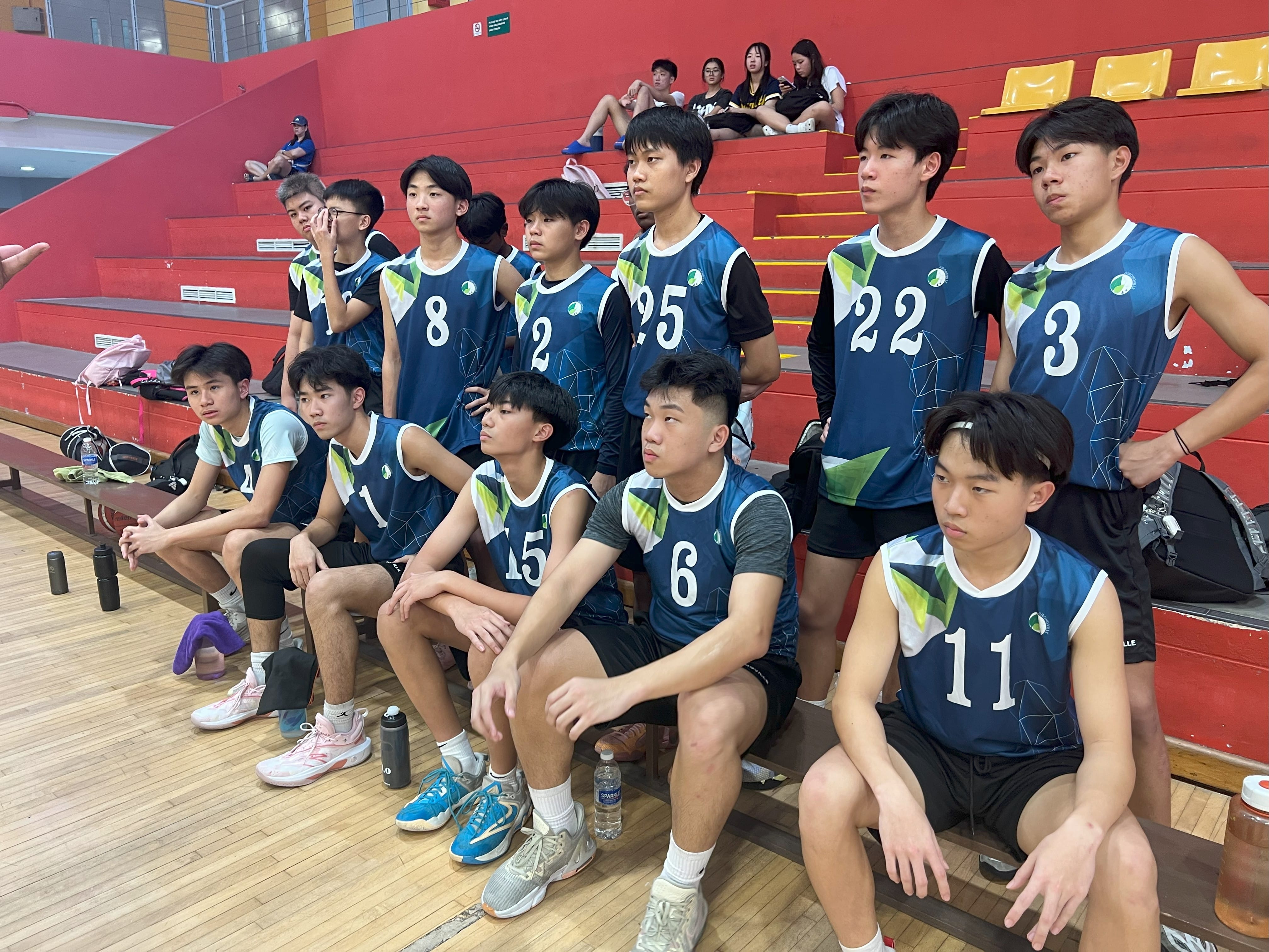 Jurongville Secondary School boys' basketball team posing together on the benches on the sidelines of an indoor sports court.