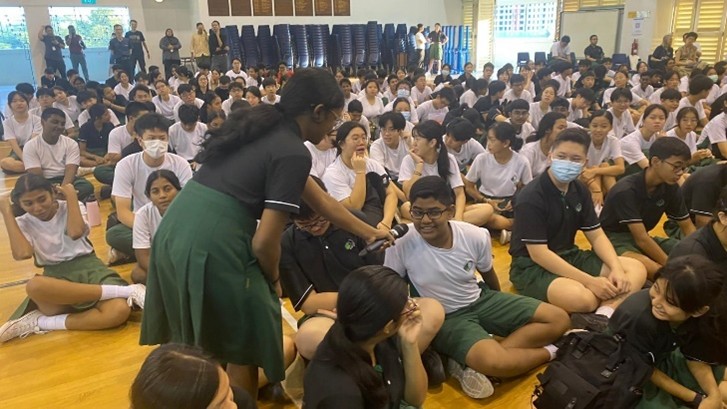An active segment of audience interaction during a cohort assembly, showing a member of the Student Council engaging directly with the student body.