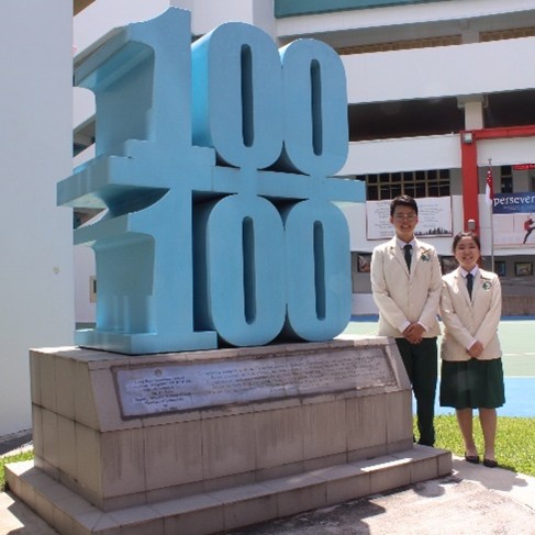 Two senior Student Leaders posing proudly alongside a prominent commemorative monument during a historical milestone or school heritage event.