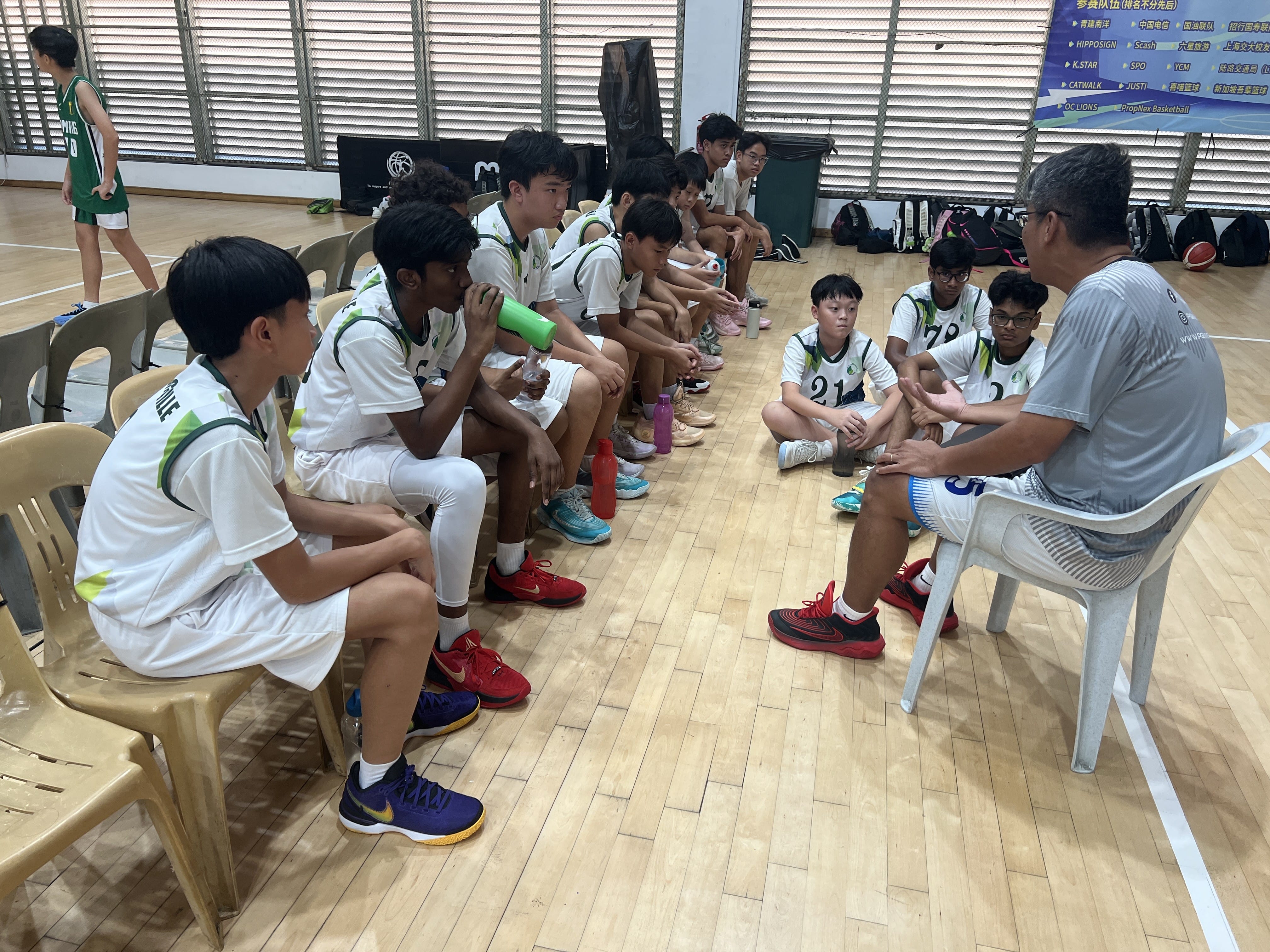 A courtside team talk or timeout briefing for the Jurongville Secondary School boys' basketball team during a tournament match.