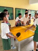 A lively, informal table tennis game set up in a school corridor, highlighting a peer engagement activity organized and managed by Sports Leaders.