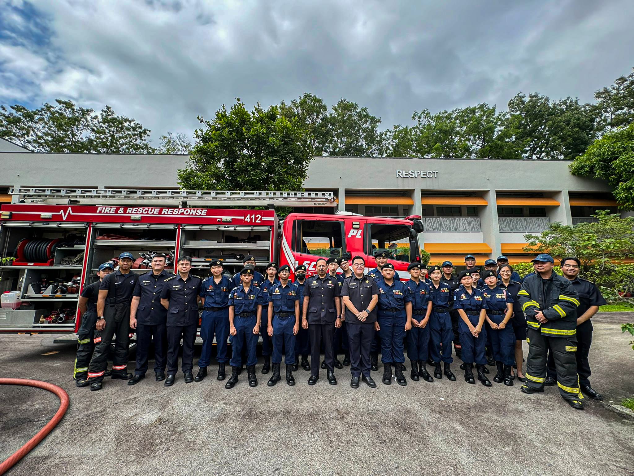 A large group of uniformed firefighters posing in front of a red Fire and Rescue Response truck numbered 412.