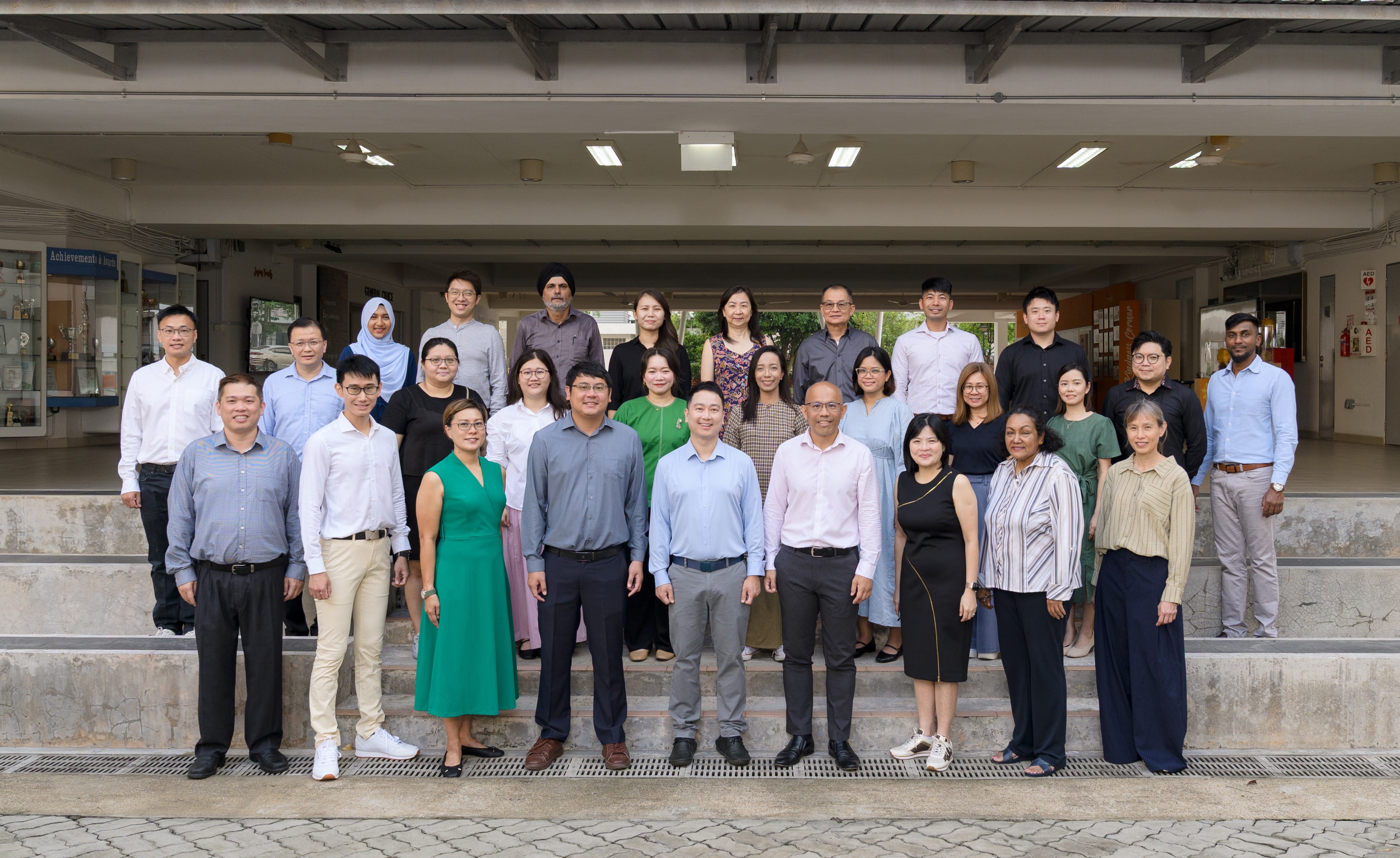 A large group of about 30 professionals posing together in three rows on steps outside a building.