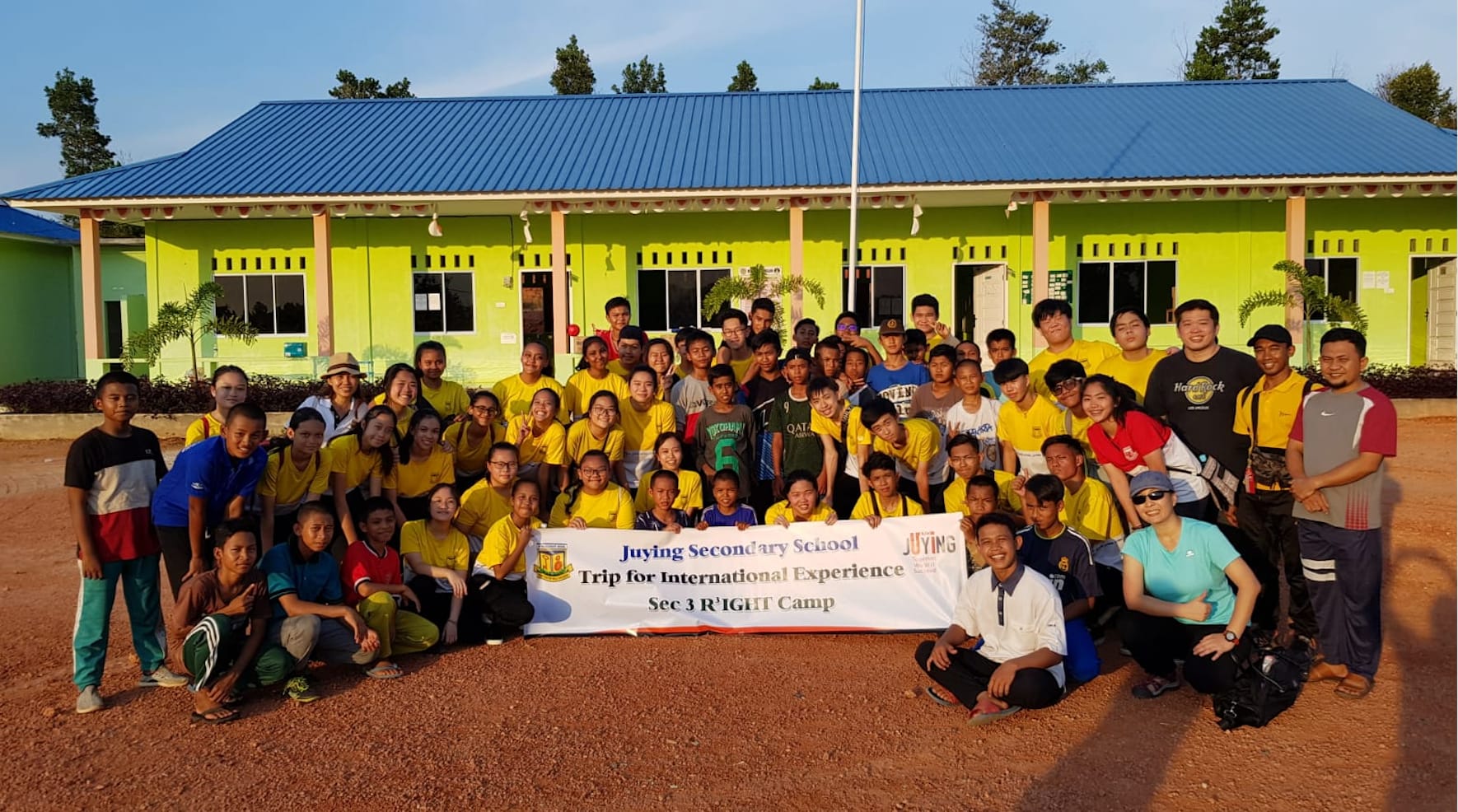 Large group of students and adults posing with a banner reading Juying Secondary School Trip for International Experience.