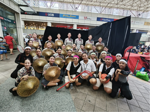 A large group of young women posing together, some holding woven bamboo hats, at a shopping mall entrance.