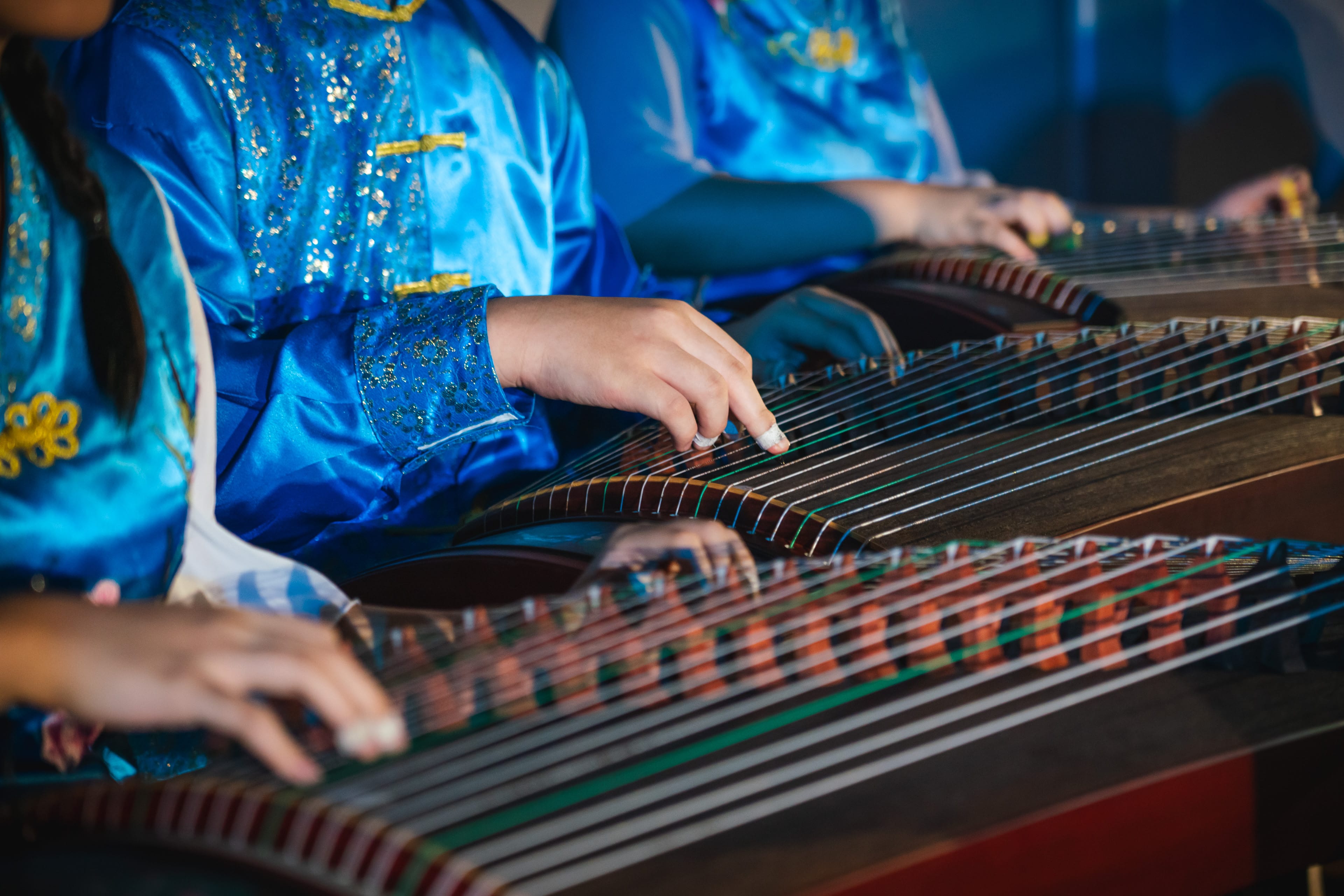Several performers in blue satin traditional Chinese costumes playing guzheng string instruments.