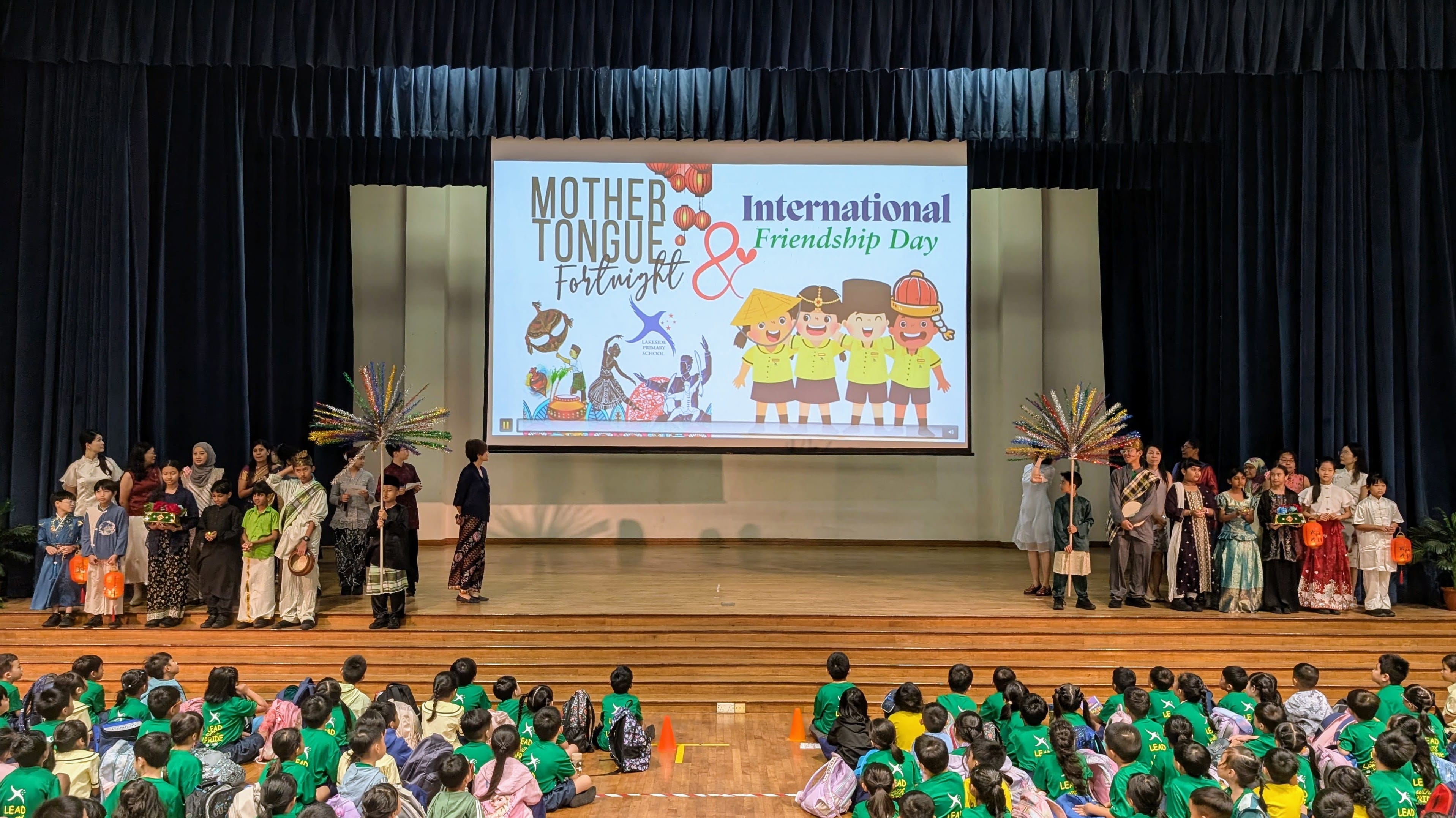 Students, staff and school leaders in cultural costumes on stage stage for the opening ceremony of the Mother Tongue Fortnight and International Friendship Day event.