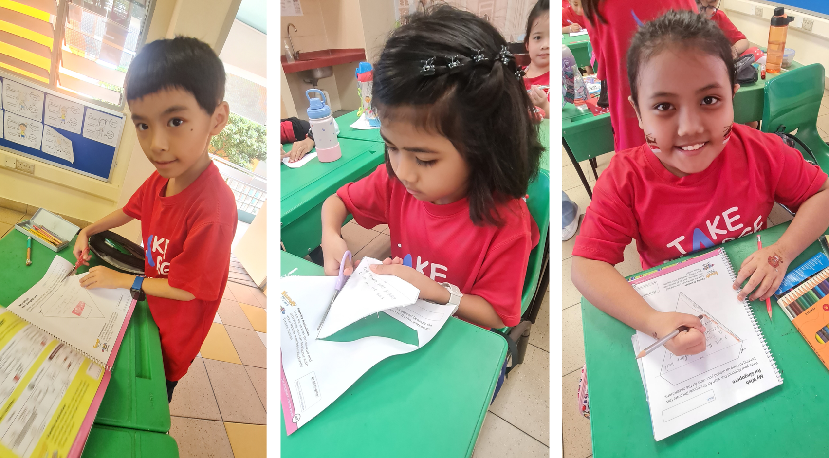 Three young children in red shirts sit at green school desks, writing or drawing in notebooks in a classroom.