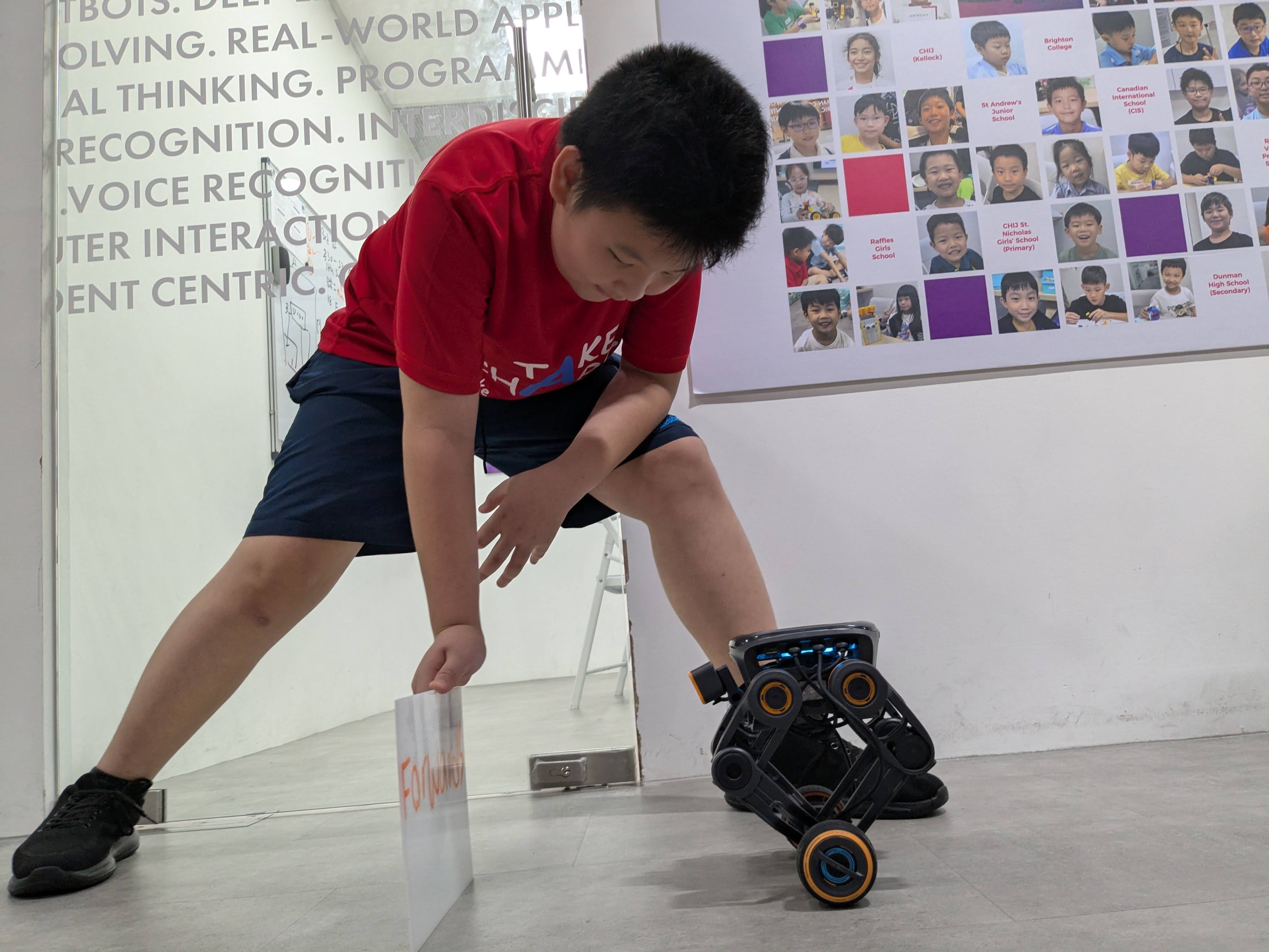 A student places a whiteboard with a word "forward" to instruct the AI Bot to move accordingly