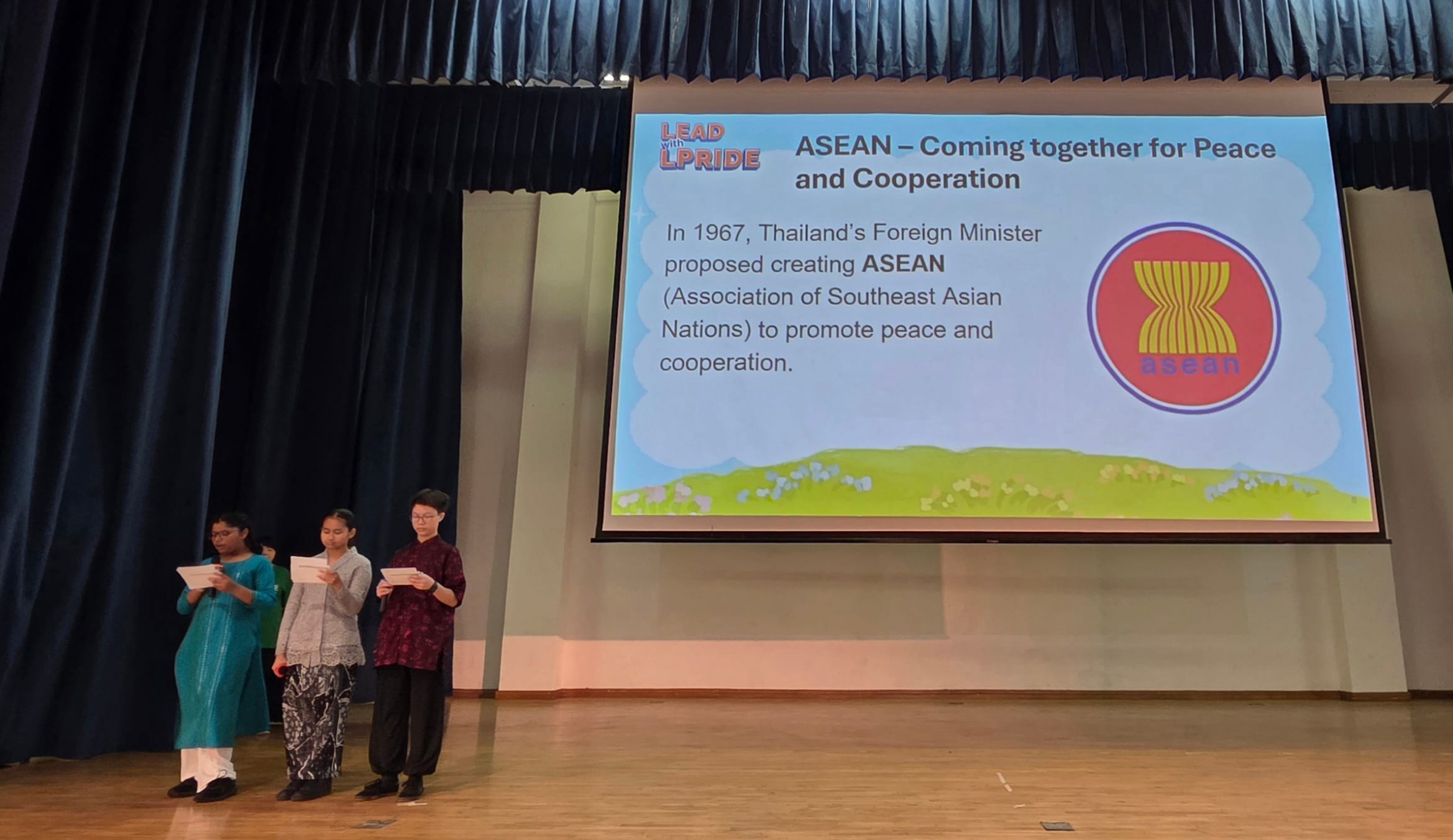 Three students emcees on stage presenting about ASEAN and peace cooperation.