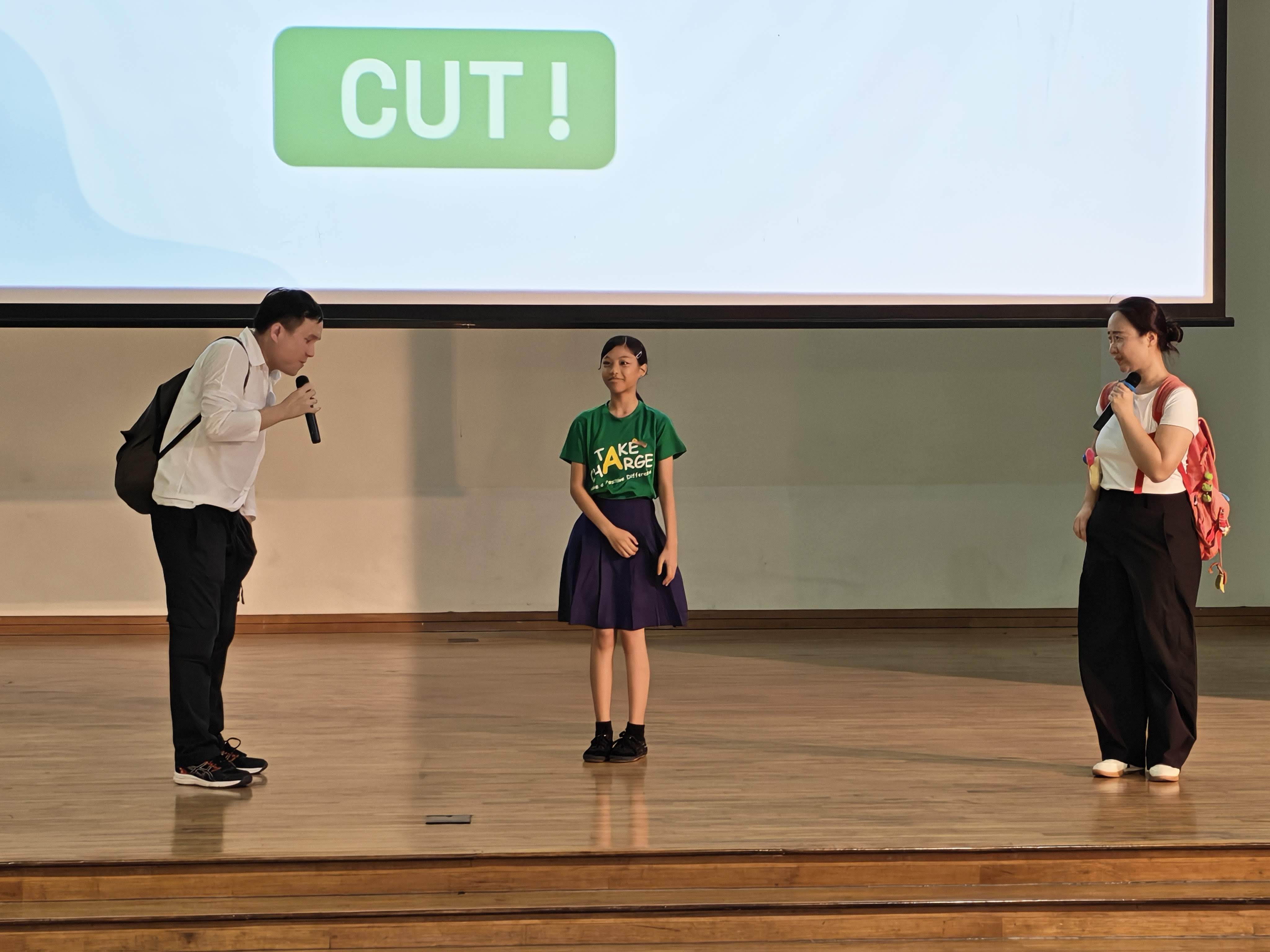 A student participates in an interactive role-play with two performers during the Racial Harmony Day assembly, helping to demonstrate the importance of understanding and respecting others.