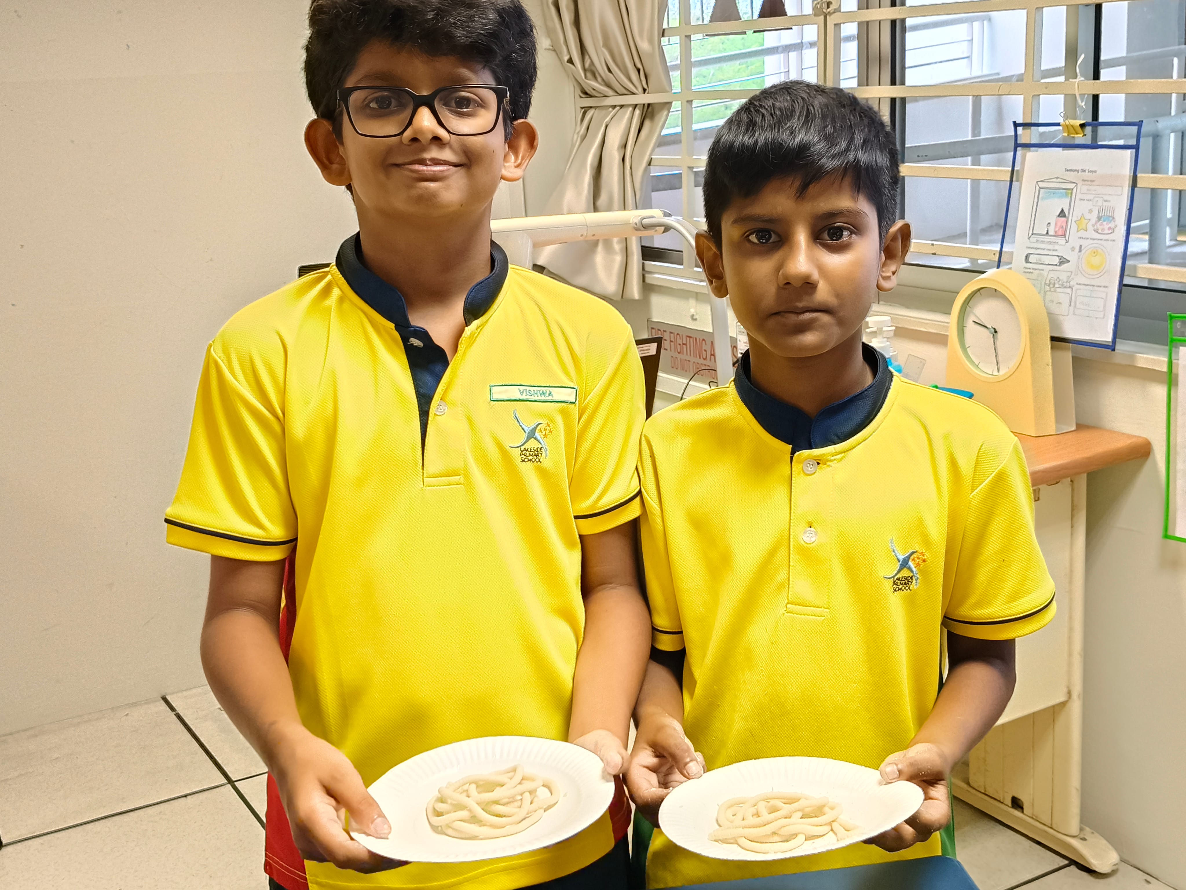 Two P6 students pose for the camera as they hold their murukku creations