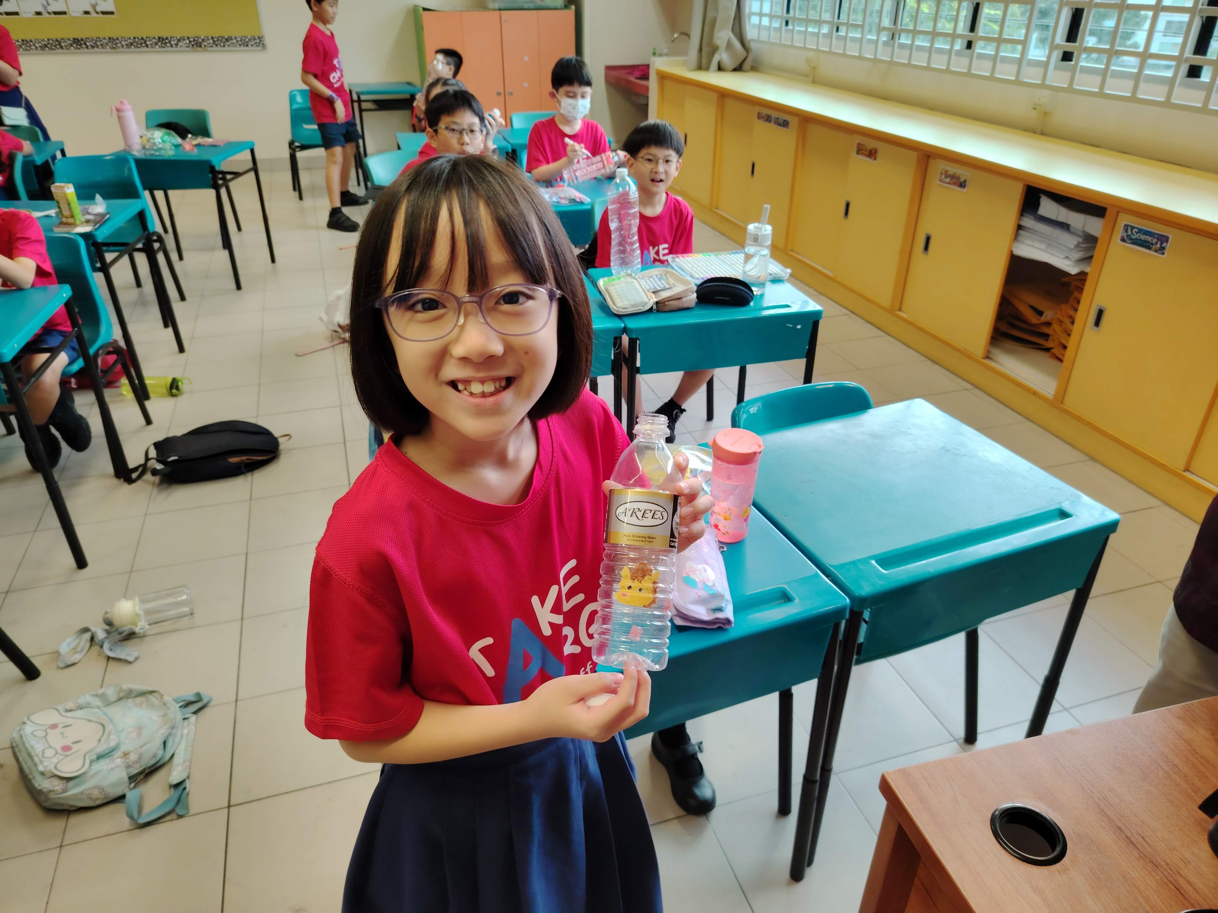 A student showcasing her handcrafted decorated instrument using "green" materials like a plastic bottle