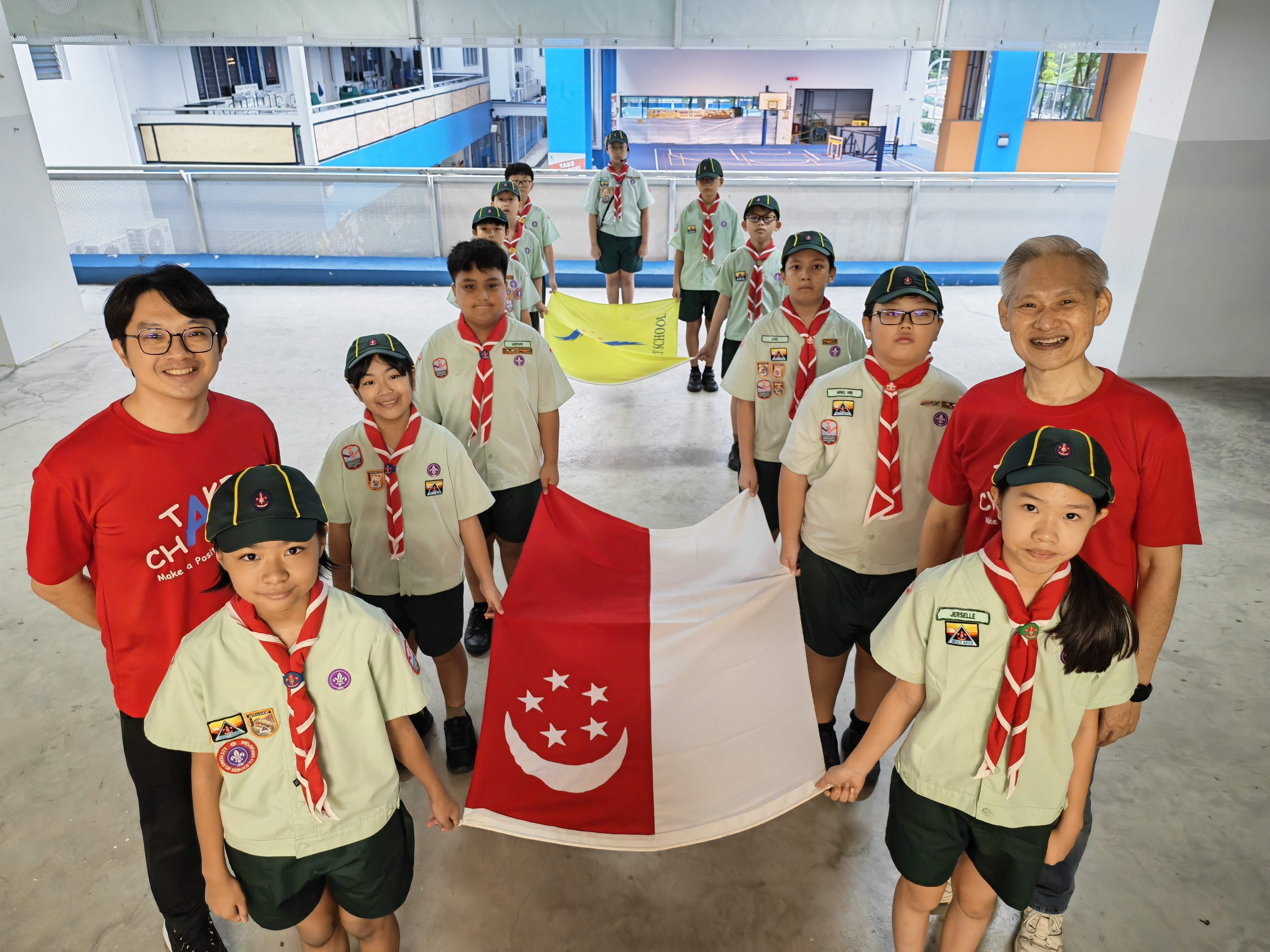 A group of Scouts and two teachers pose together while holding a large Singapore flag as they prepare for the school’s National Day Observance Ceremony.