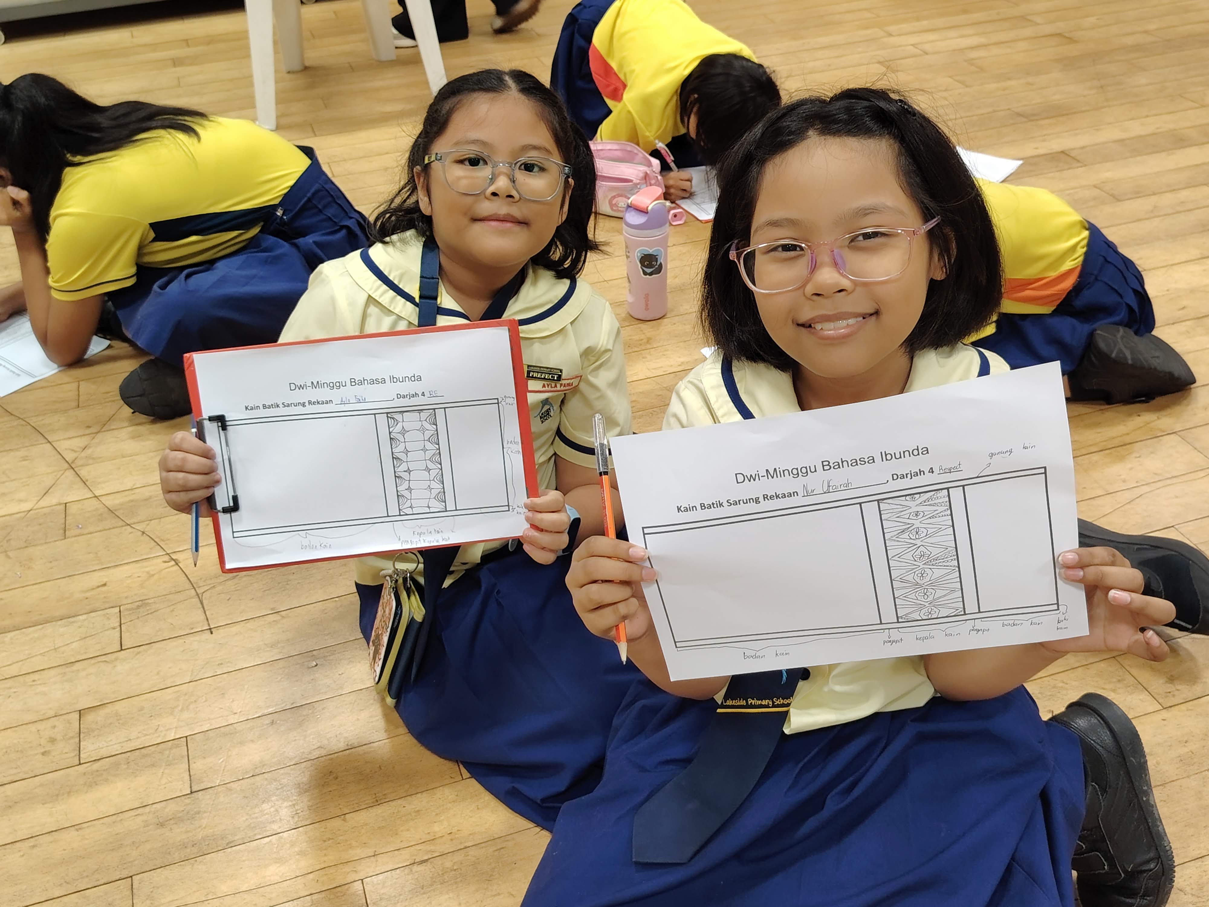 P4 students proudly displaying their hand-drawn batik motifs