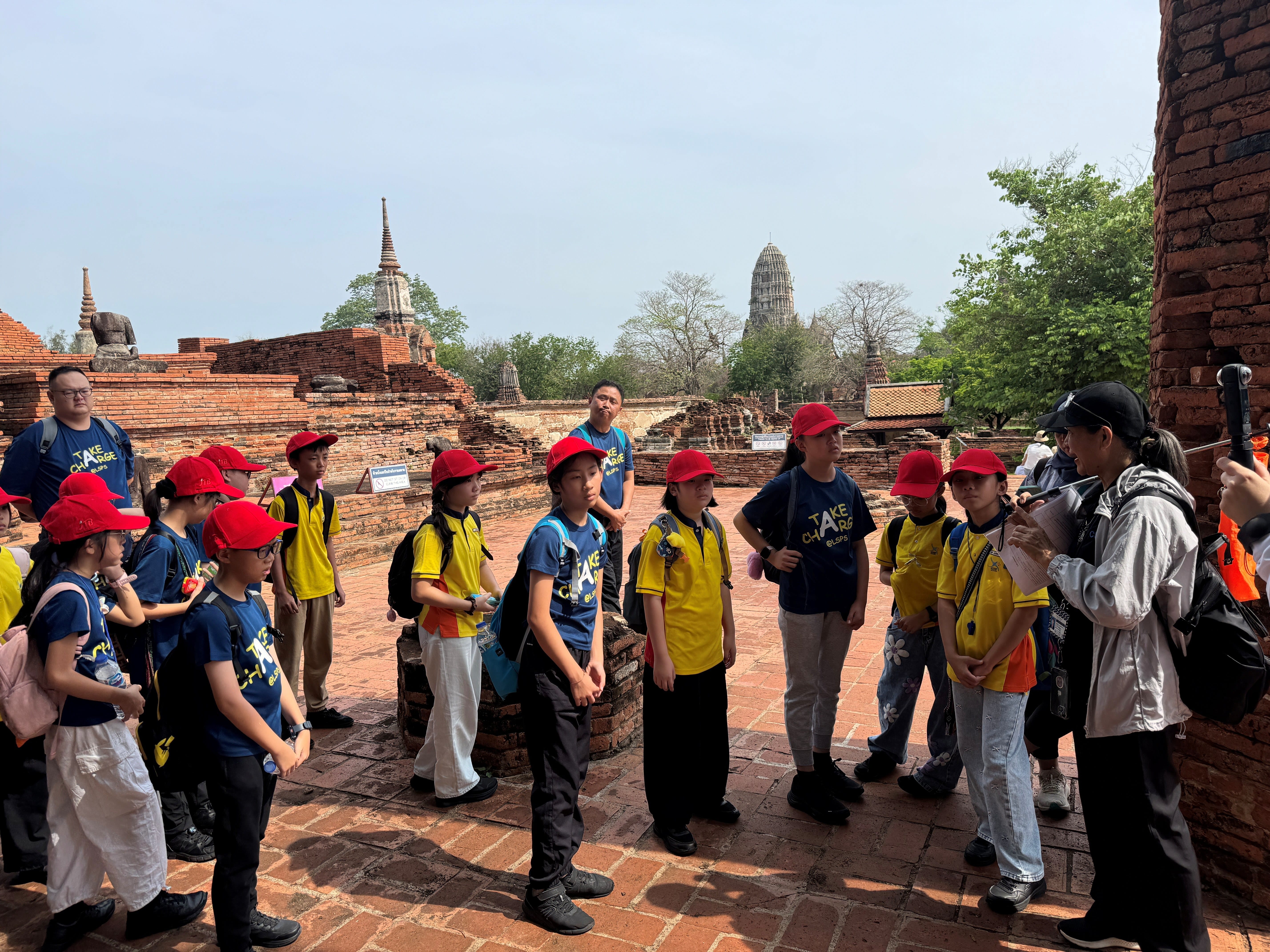 Students in red cap gathered in front of the host as she explains the history and cultural significance of the place in Bangkok