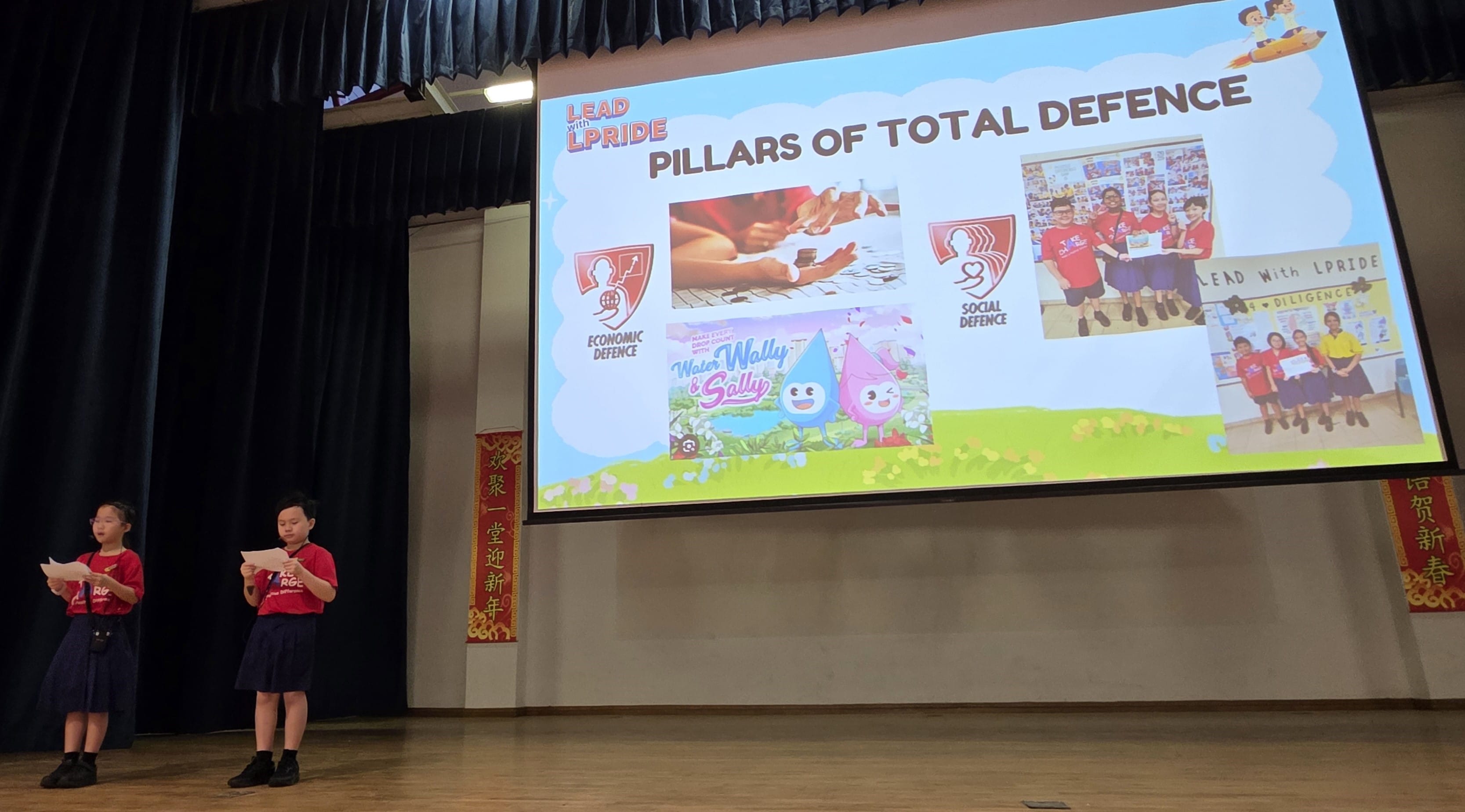Our two student leaders on stage facilitating the Total Defence Day presentation during PAVE