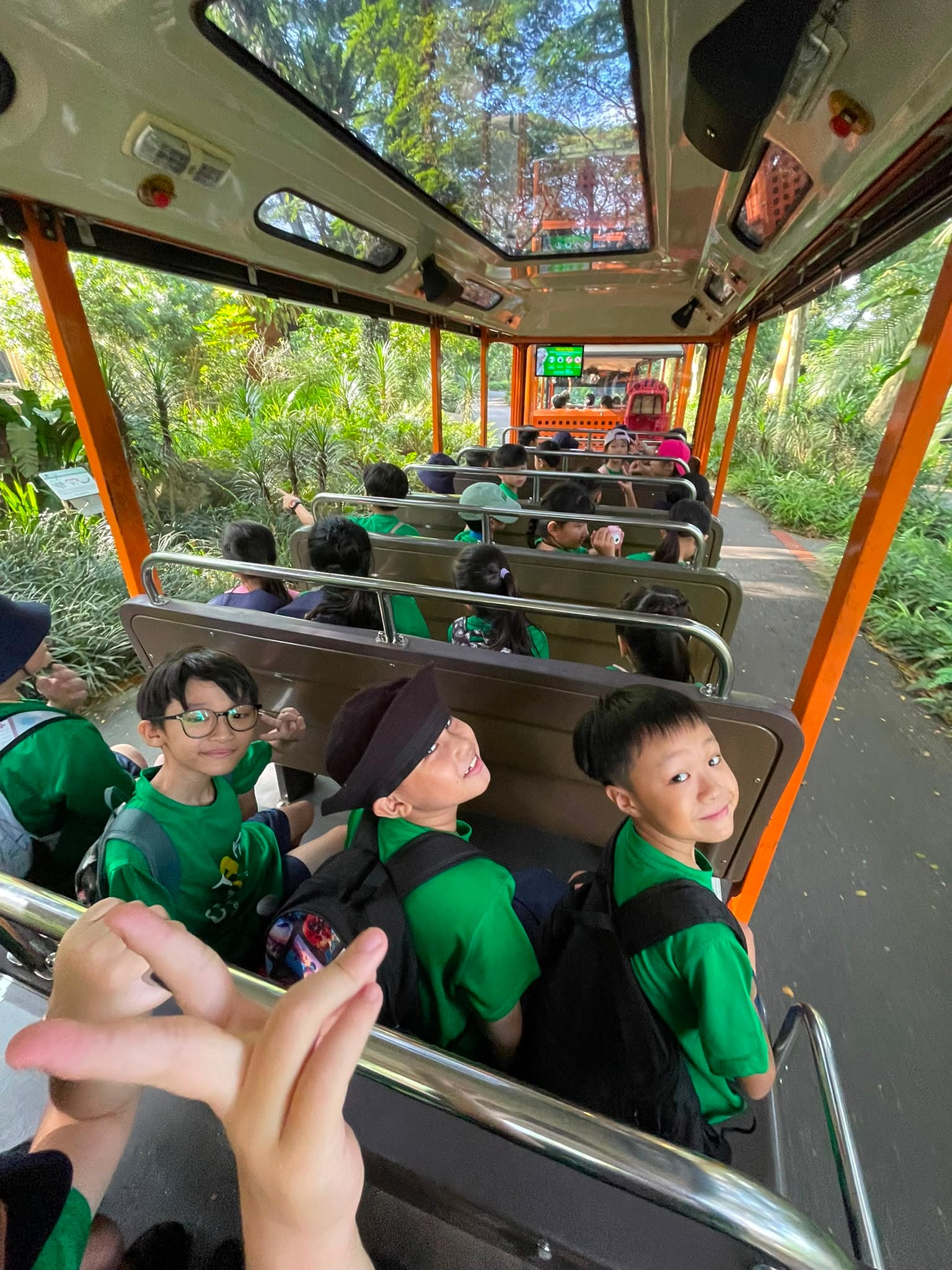 Students in green "Take Charge" T-shirts seated on a zoo tram, travelling through a lush green path.