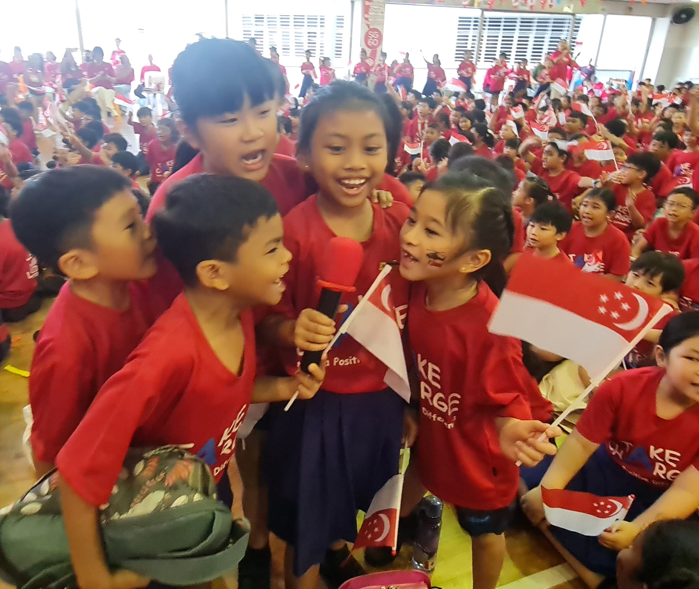 Students sing proudly into the microphone in a spirited community sing-along led by the teachers and the choir