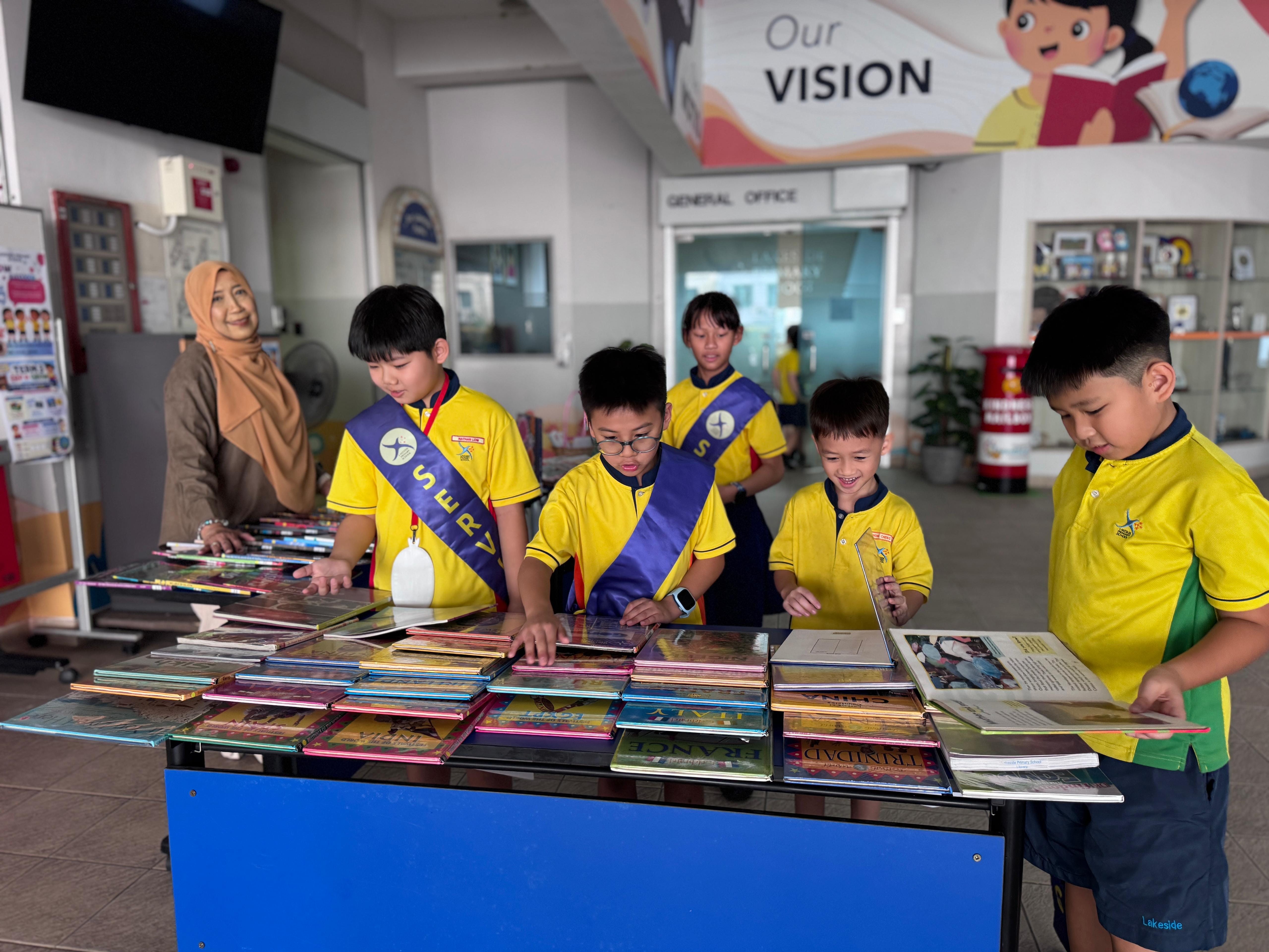 Students browse a selection of books on racial harmony and multiculturalism during a recess reading activity, choosing titles to borrow and enjoy.