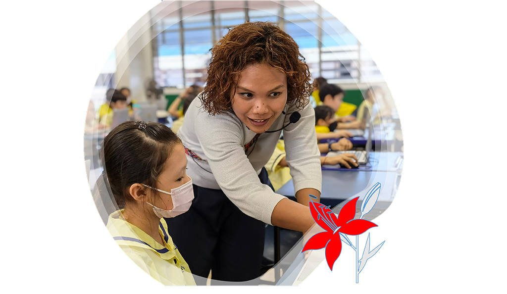 Mrs Ain Lager leans over to guide a student , pointing at the student's work on a desk in a classroom.