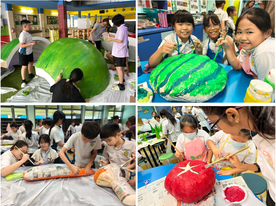 Children paint large papier-mache vegetable and fruit sculptures including a watermelon, carrot, and tomato during a school art activity.