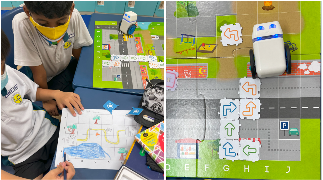Two masked children use arrow tiles to program a small robot on a colorful grid map during a coding activity.