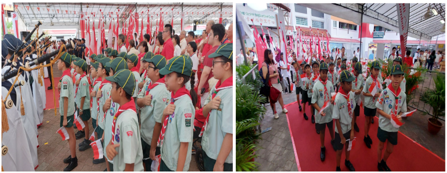 Young scouts in green uniforms and hats stand in formation and march along a red carpet at an outdoor event.