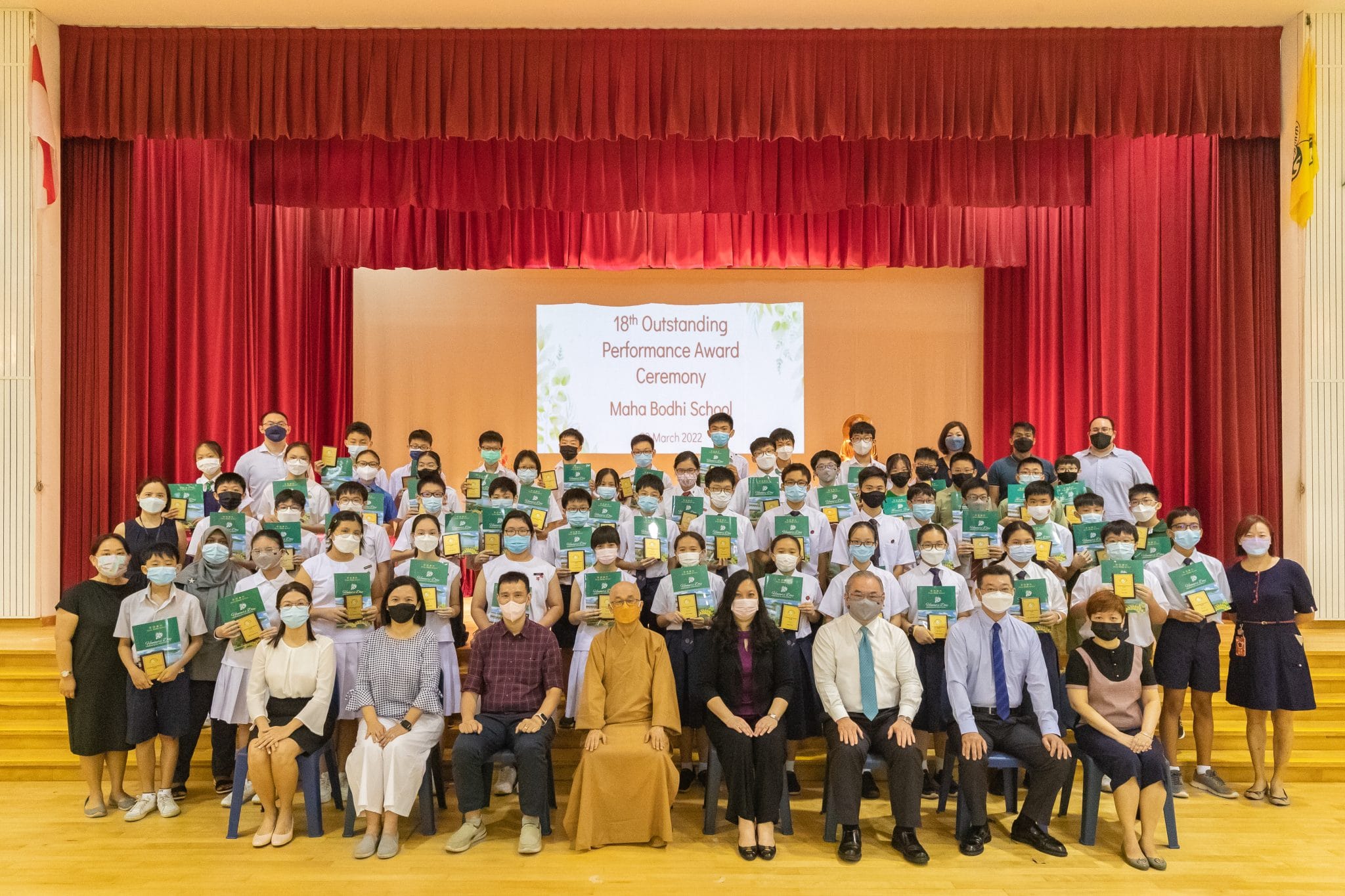 Large group of masked students and staff pose with awards at Maha Bodhi School's 18th Outstanding Performance Award Ceremony.