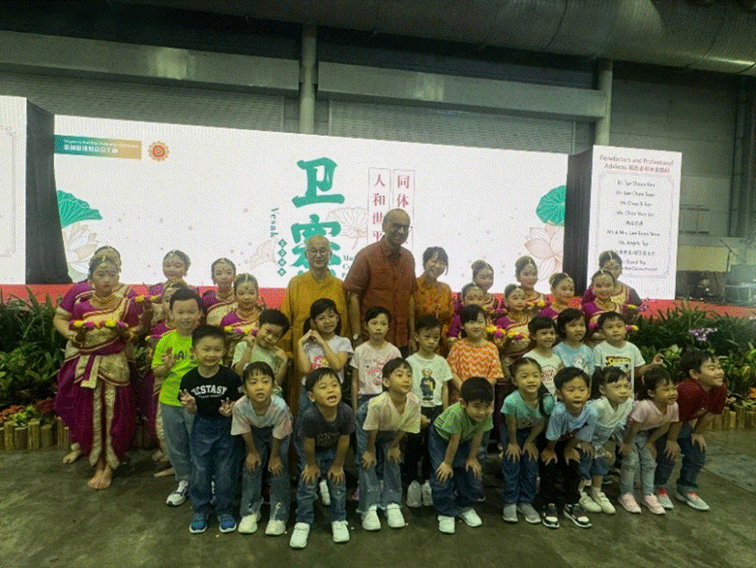 A group of young children and adults pose in front of a Chinese banner, with girls in colorful traditional costumes on the sides.
