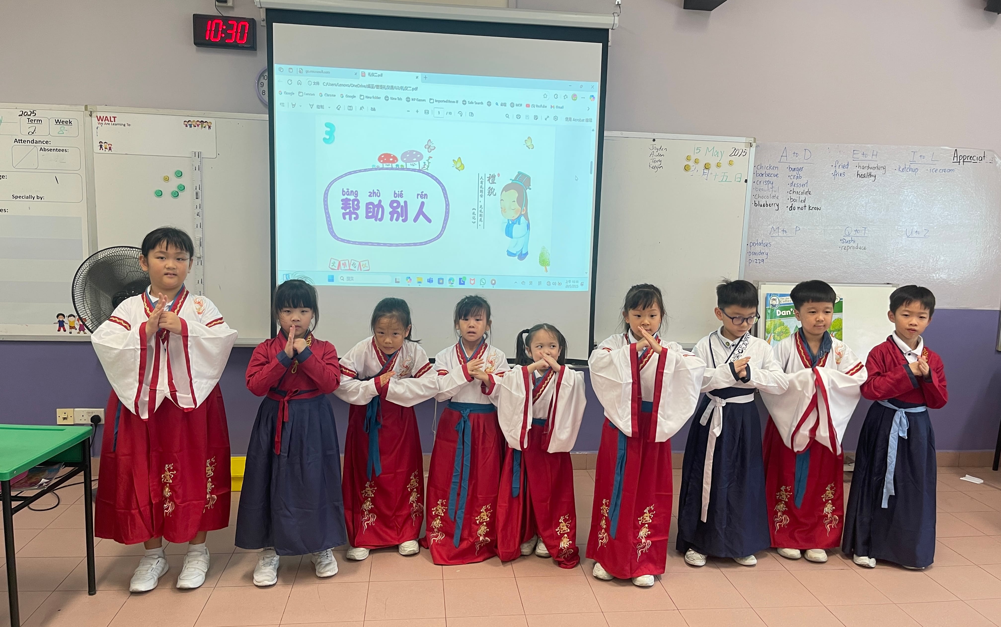 Eight children in traditional Chinese hanfu clothing stand in a classroom, performing a bow gesture in front of a projected screen.