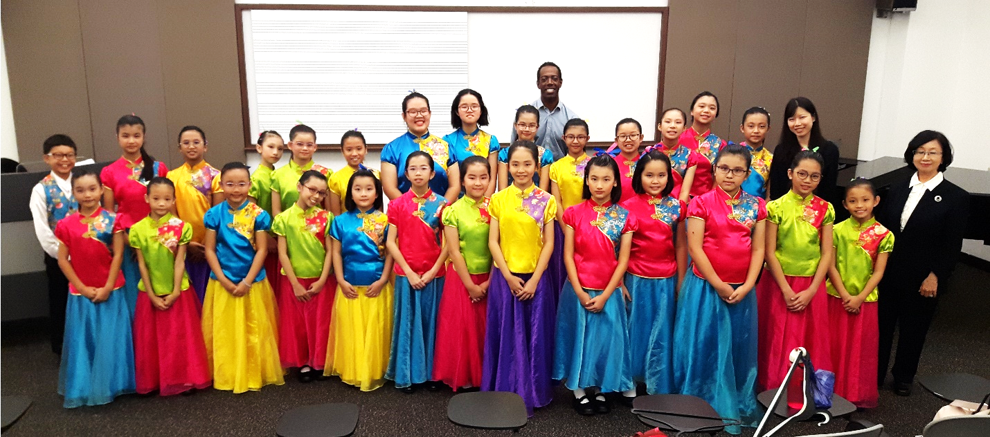 A large group of children in colorful traditional Chinese costumes pose with two adults in a classroom.