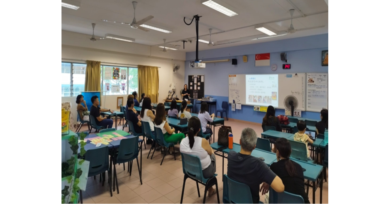 A teacher stands at the front of a classroom presenting slides to parents during Afternoon with Teacher.