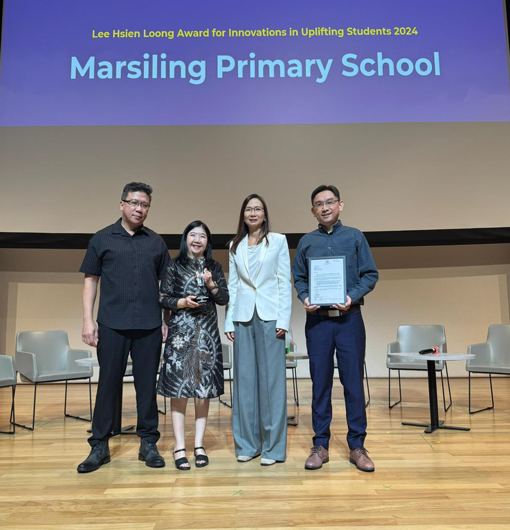 Marsiling Primary School staff on stage receiving the 2024 LHL Award trophy and certificate.