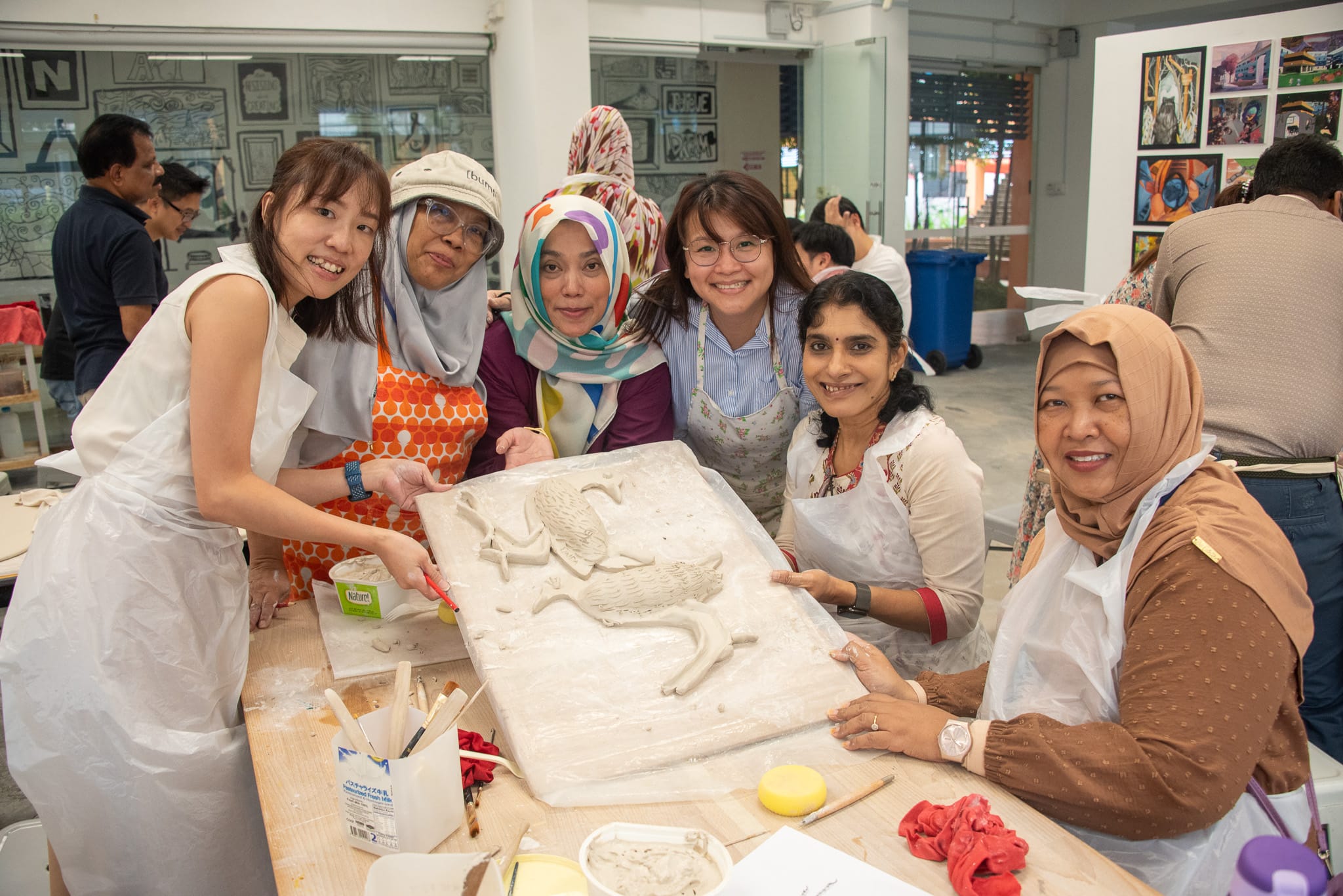 Five smiling women in aprons pose around a clay relief sculpture of a horse in an art studio.