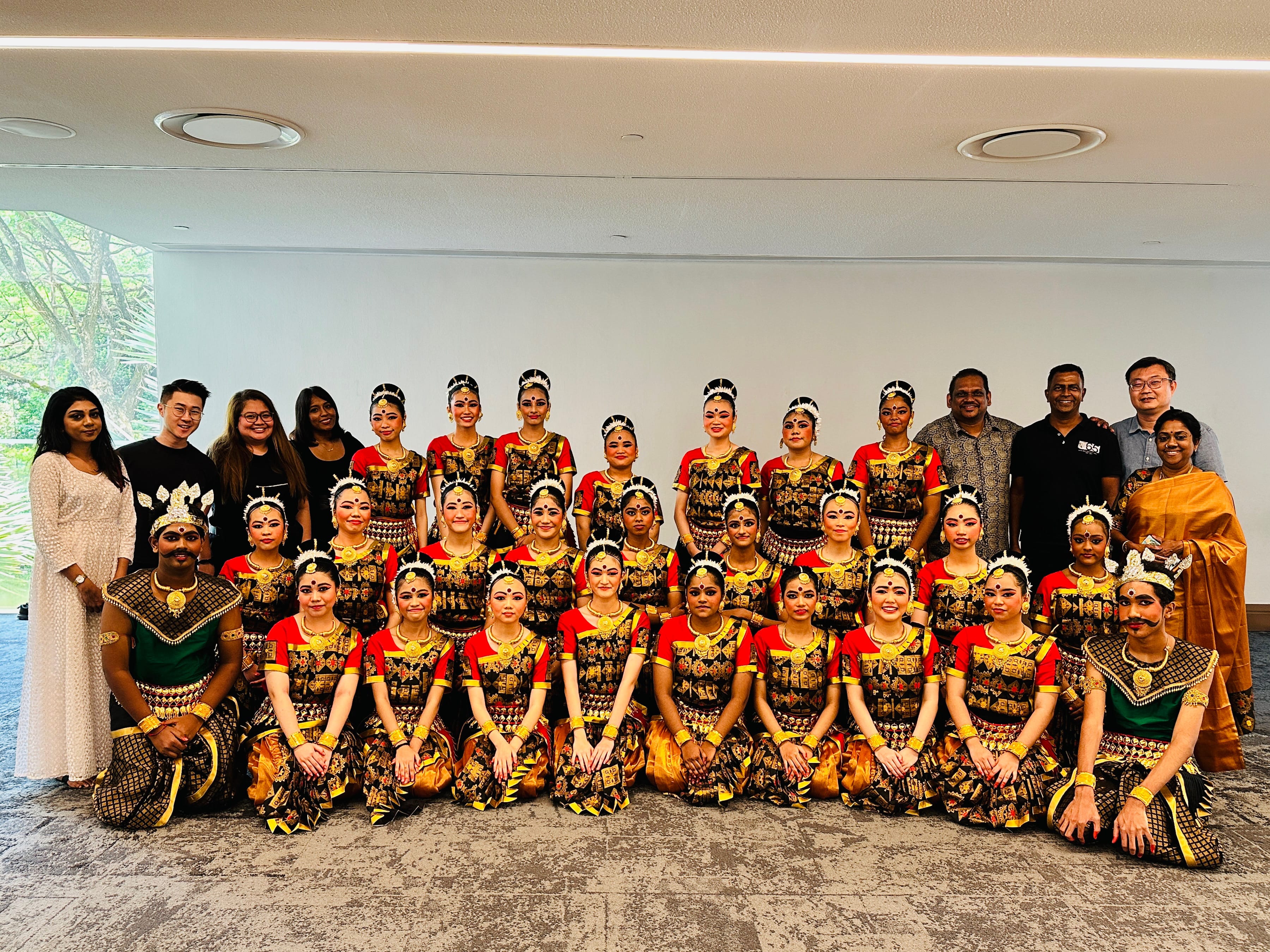 Large group photo of dancers in matching red, gold, and black costumes, with several adults behind them.