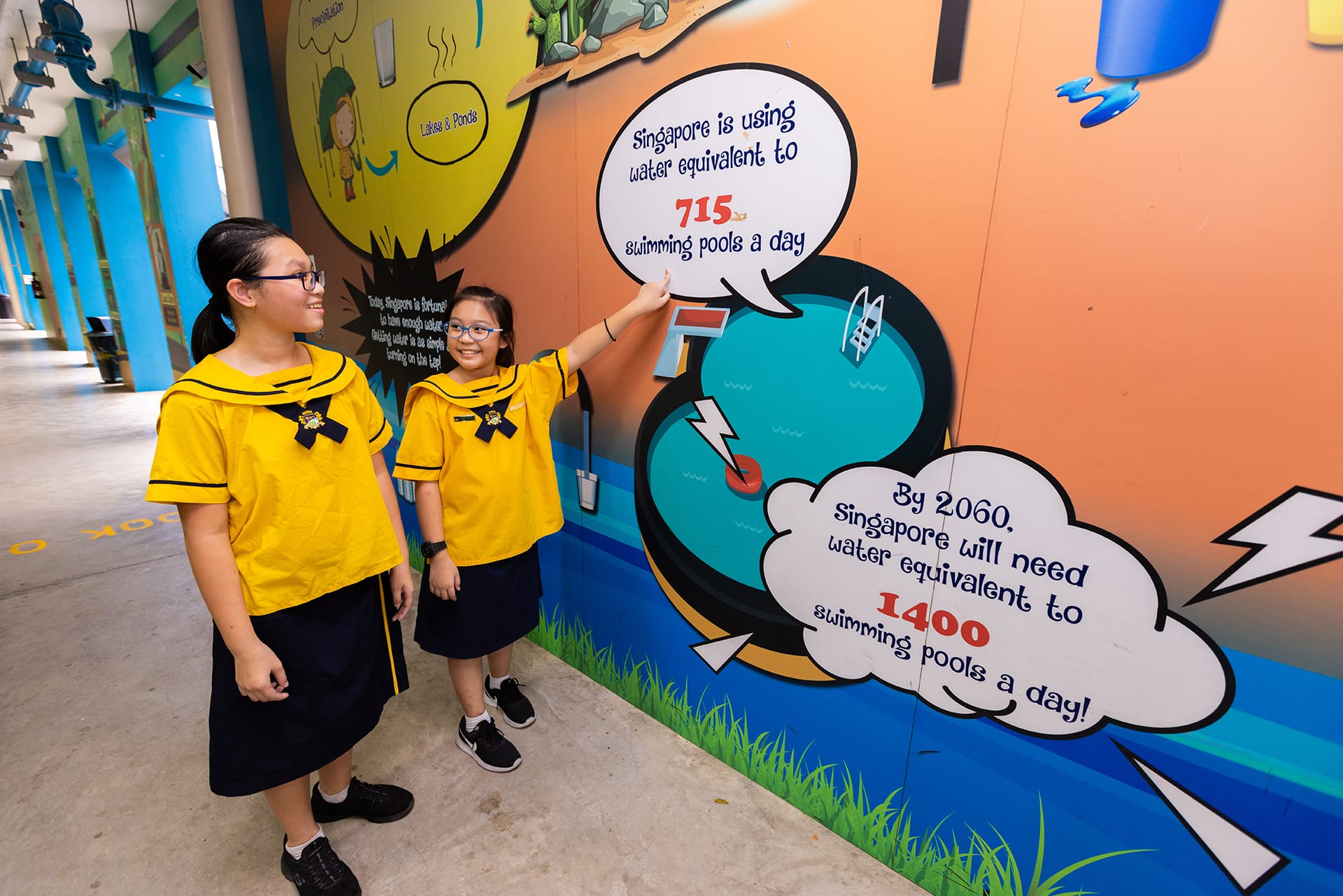 Two girls in yellow school uniforms point at a colorful mural about Singapore's water usage statistics.