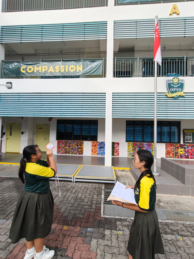 Two students standing at the parade square attempting to measure the height of the flag pole using a clinometer