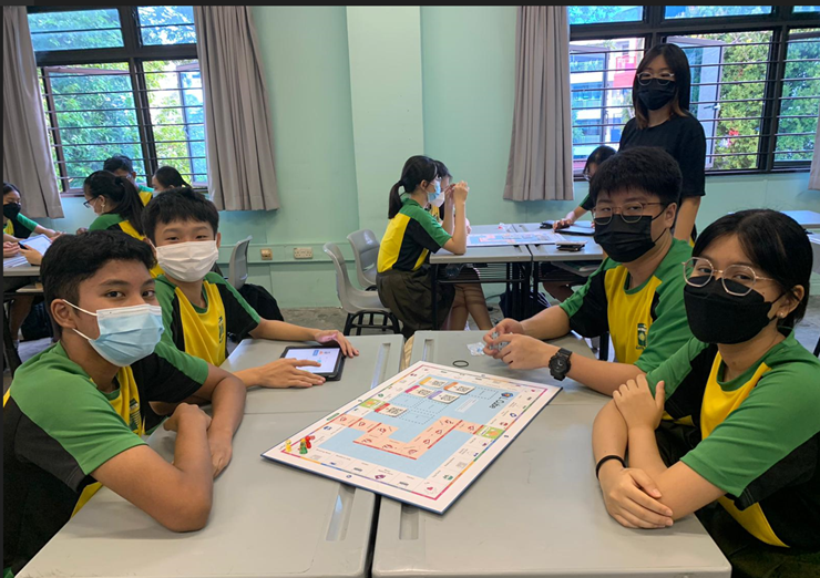 Four students seated on opposite sides of the table with a financial literacy board game between them