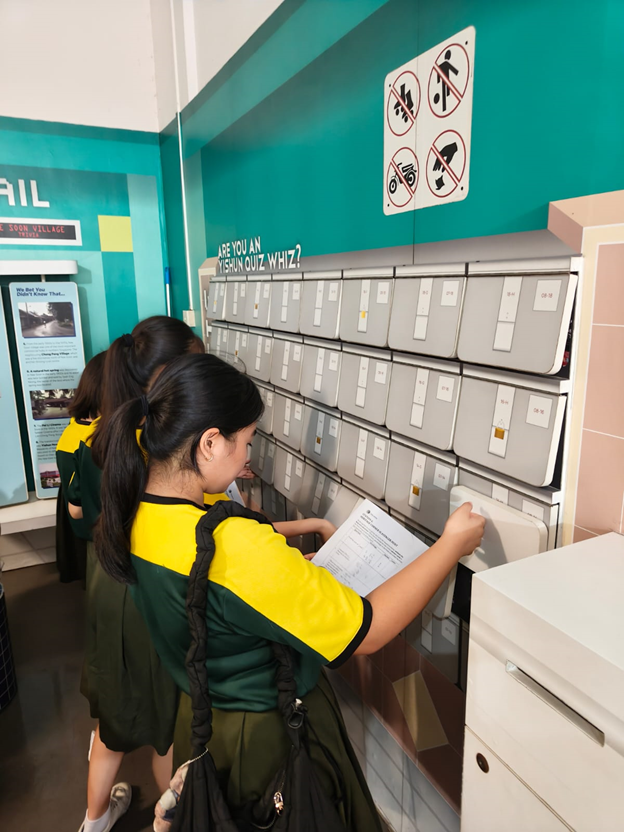A group of students standing by a mock old-school letter boxes, solving a mathematical puzzle.