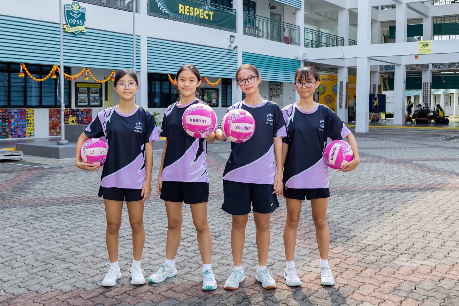 A group of 4 netball girls posing for a shot with their netballs