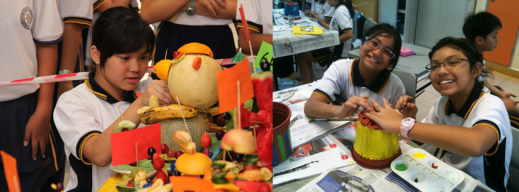 Students in white uniforms work on creative projects: one arranges a fruit sculpture, two others smile while crafting a decorated structure.