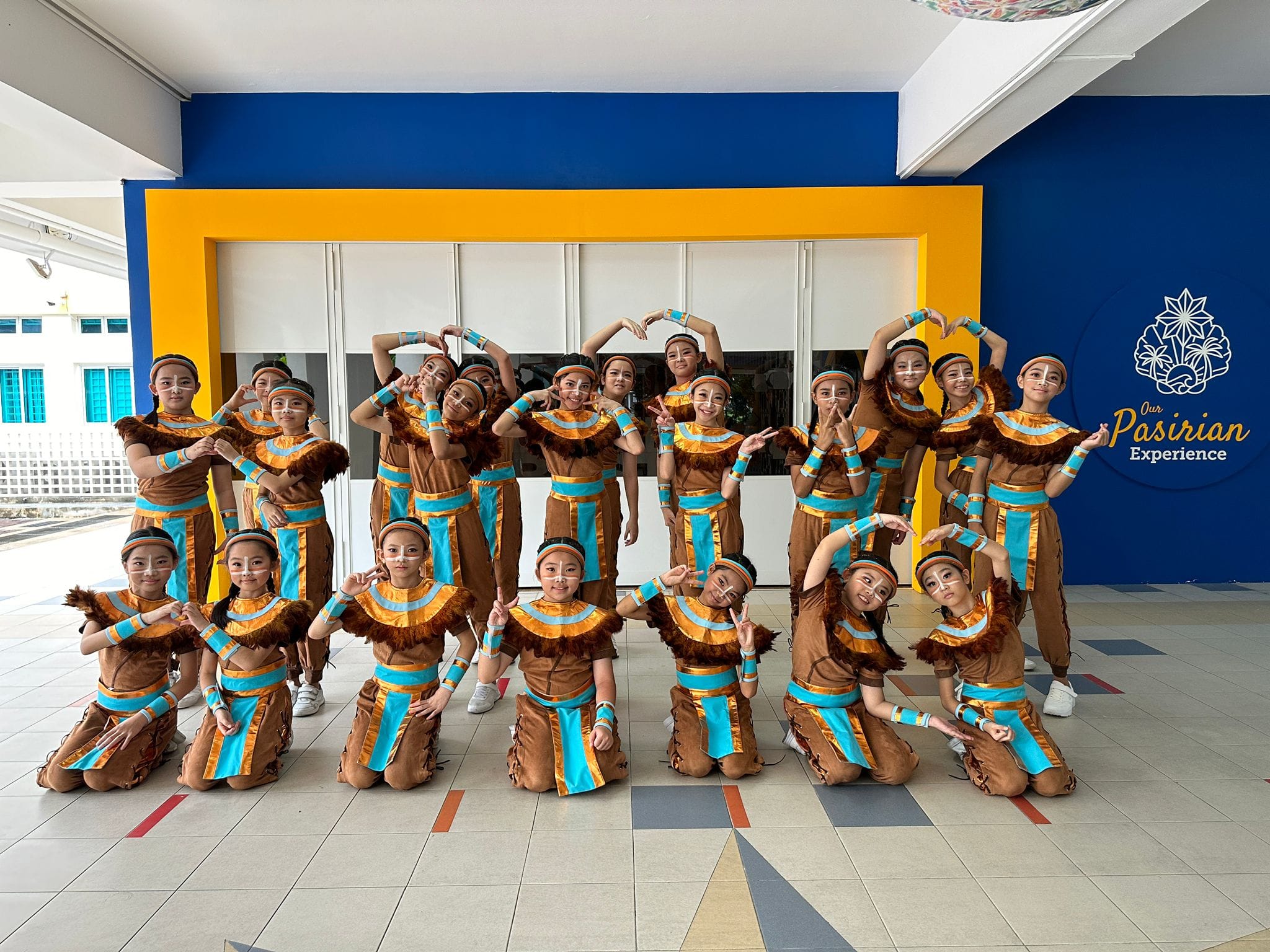 A group of children in matching brown and turquoise tribal costumes pose together at a Pasirian Experience event.
